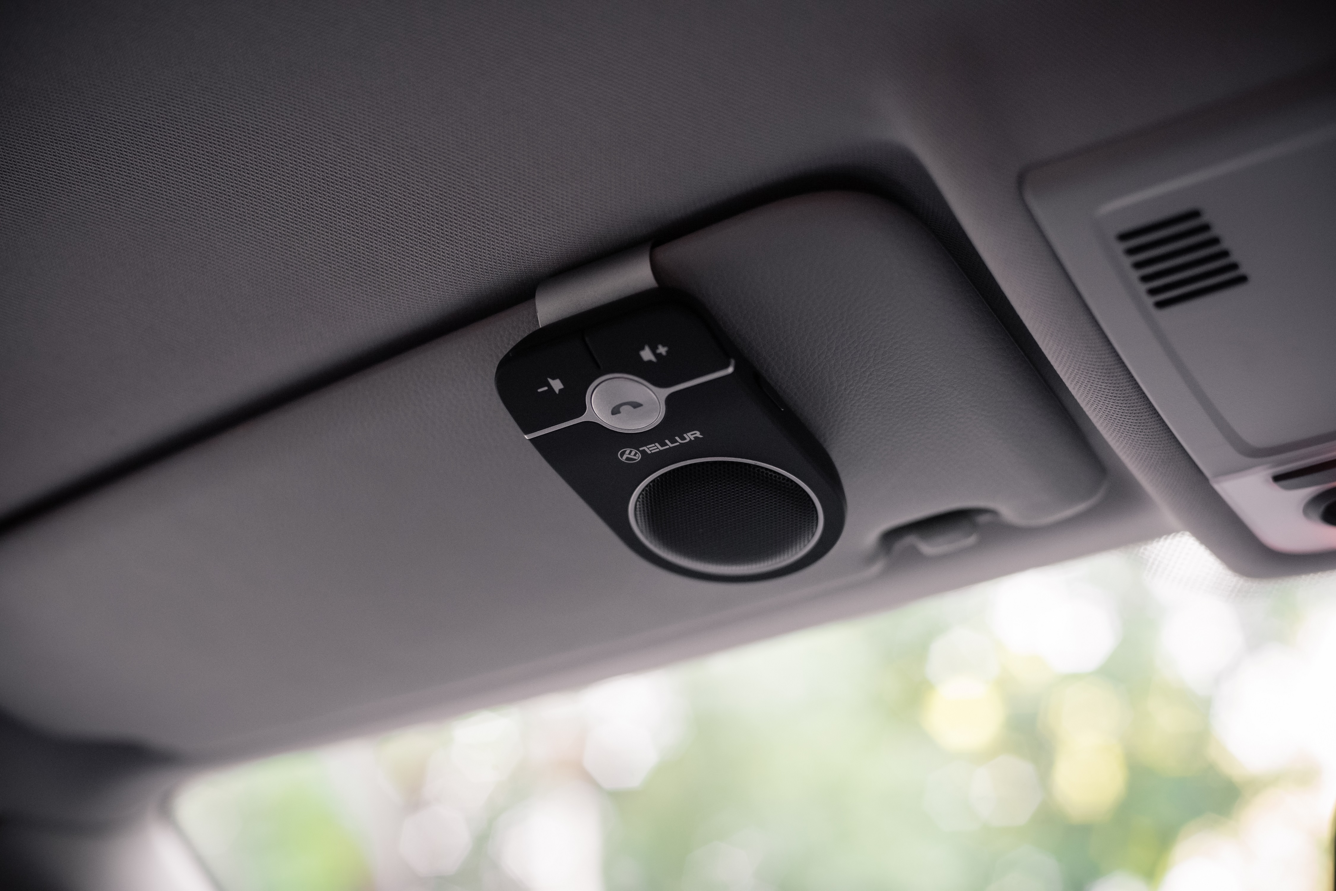 Altavoz de coche negro sujeto a una visera. Visera gris y techo del coche visibles.