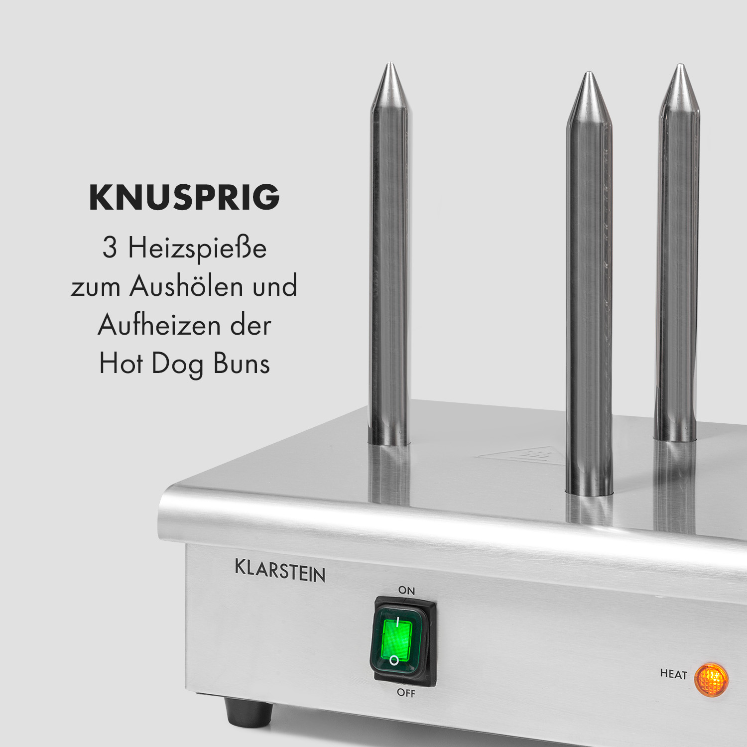 Nahaufnahme eines Hotdog-Brötchenwärmers mit drei Metallspitzen und einem grünen Einschaltknopf.