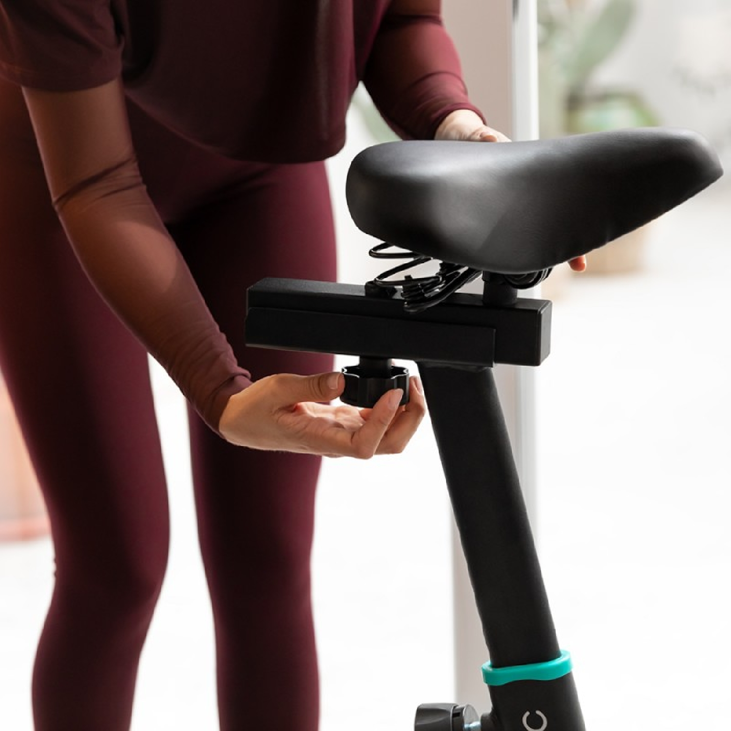 Una persona sta regolando il sedile di una cyclette. Il sedile è nero e la bici è nera e turchese.