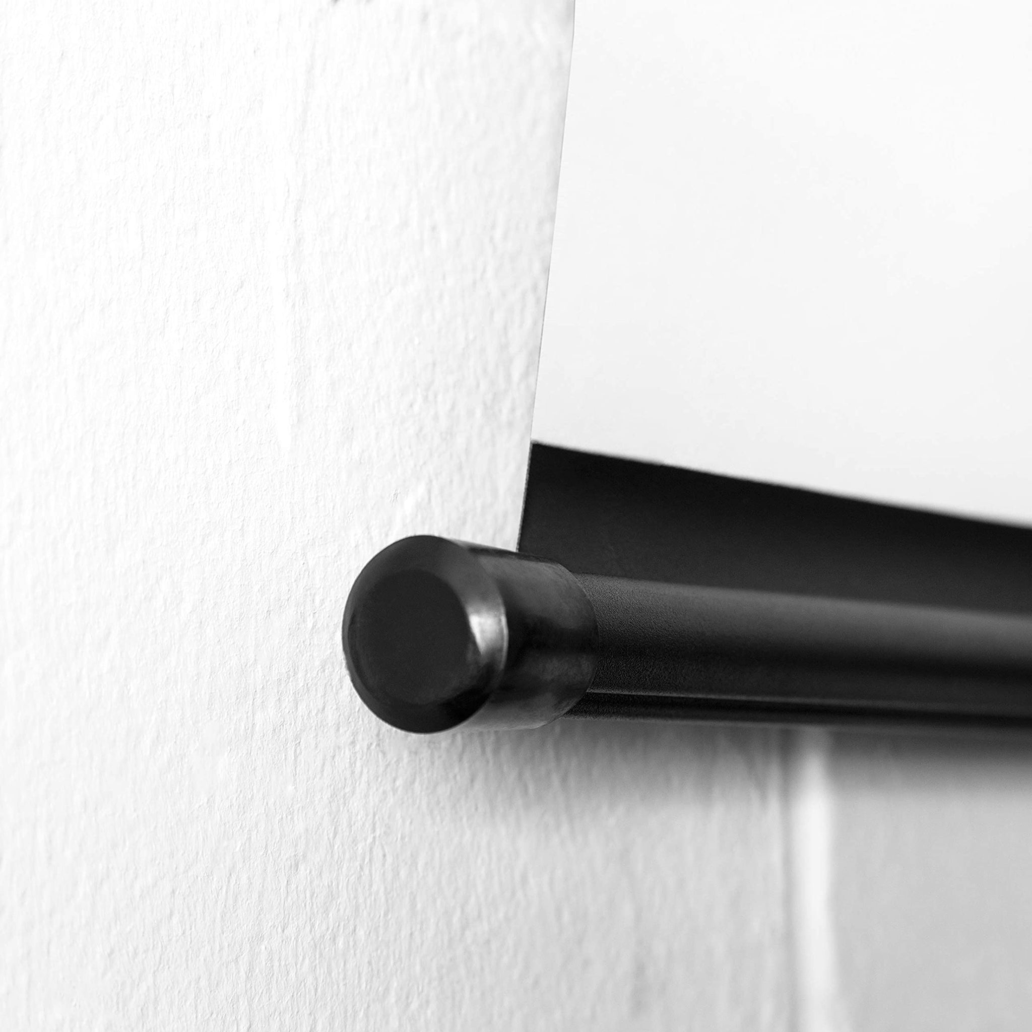 Nahaufnahme einer schwarzen Rollenleiste mit weißem Papier, das von ihr an einer weißen Wand hängt.
