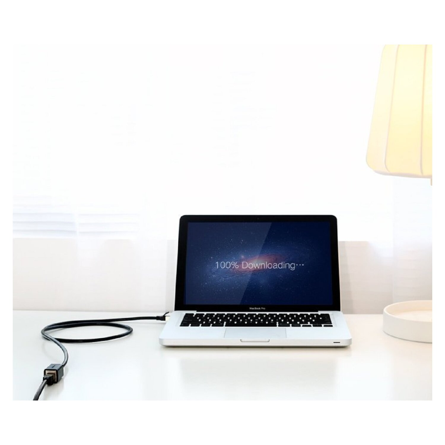 Laptop na białym biurku, 100% pobierania na ekranie. Czarny kabel.