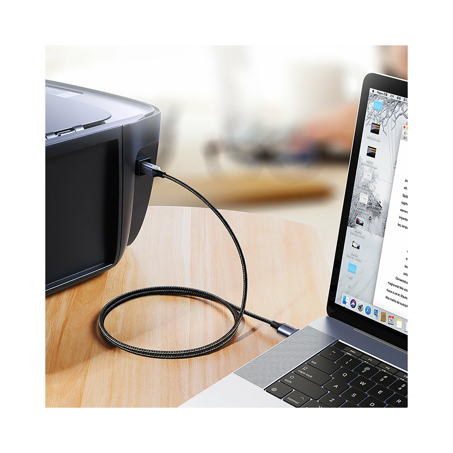 Laptop mit Kabel an Drucker angeschlossen. Ein Holztisch ist im Vordergrund.