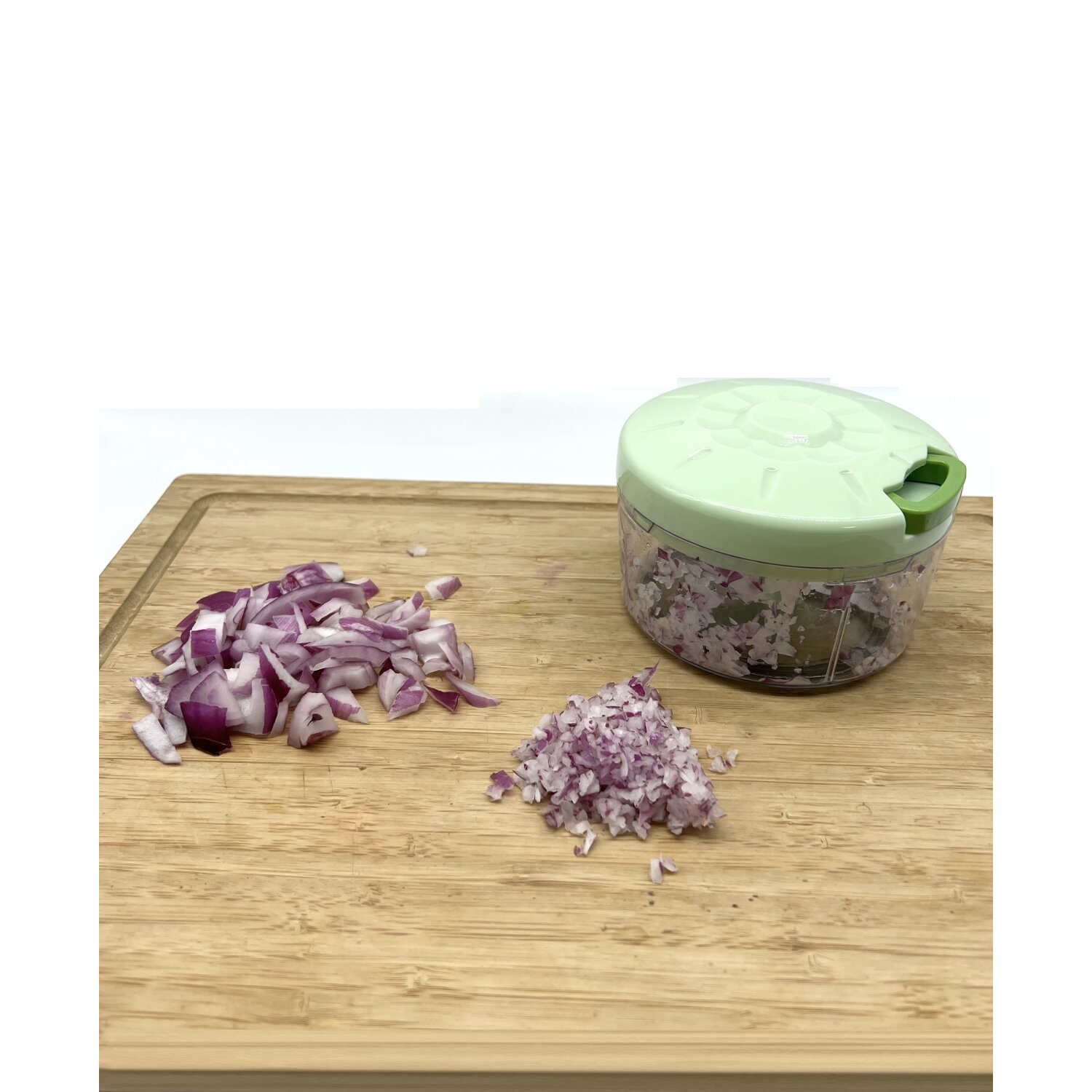 Gehackte rote Zwiebeln auf einem Holzbrett neben einem grünen manuellen Zerkleinerer.
