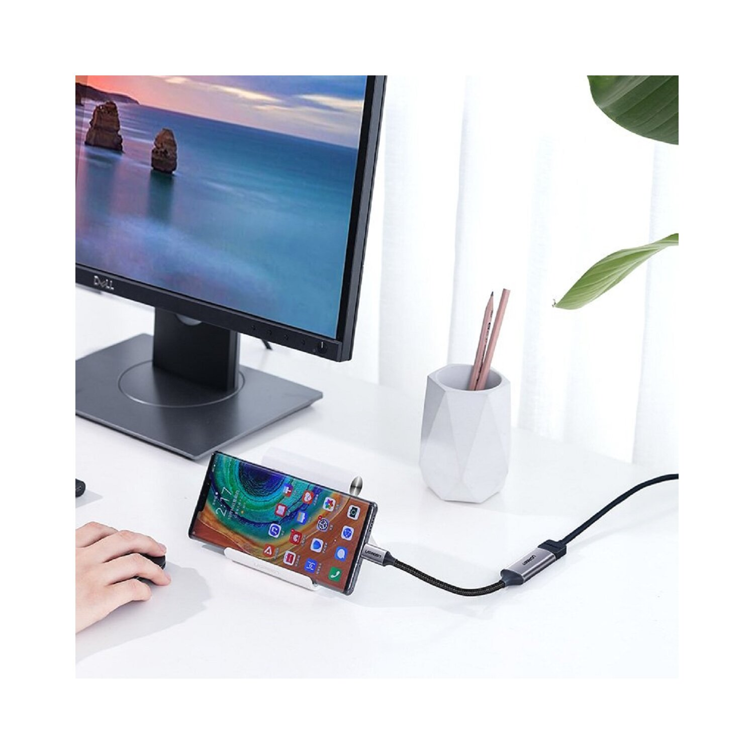 Smartfon podłączony do monitora. Białe biurko z pojemnikiem na długopisy. Ciemne tło.