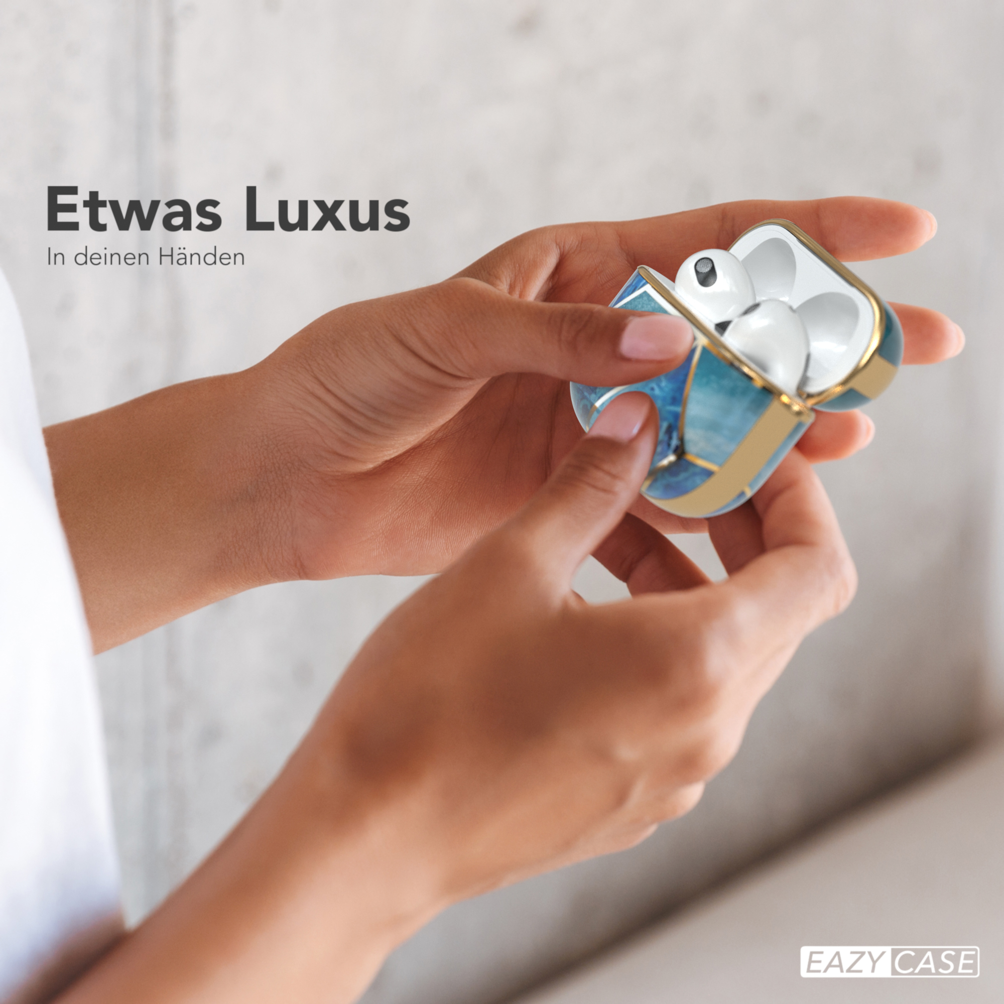 Hände halten ein offenes, goldverziertes, blau gemustertes AirPods-Etui mit AirPods darin.