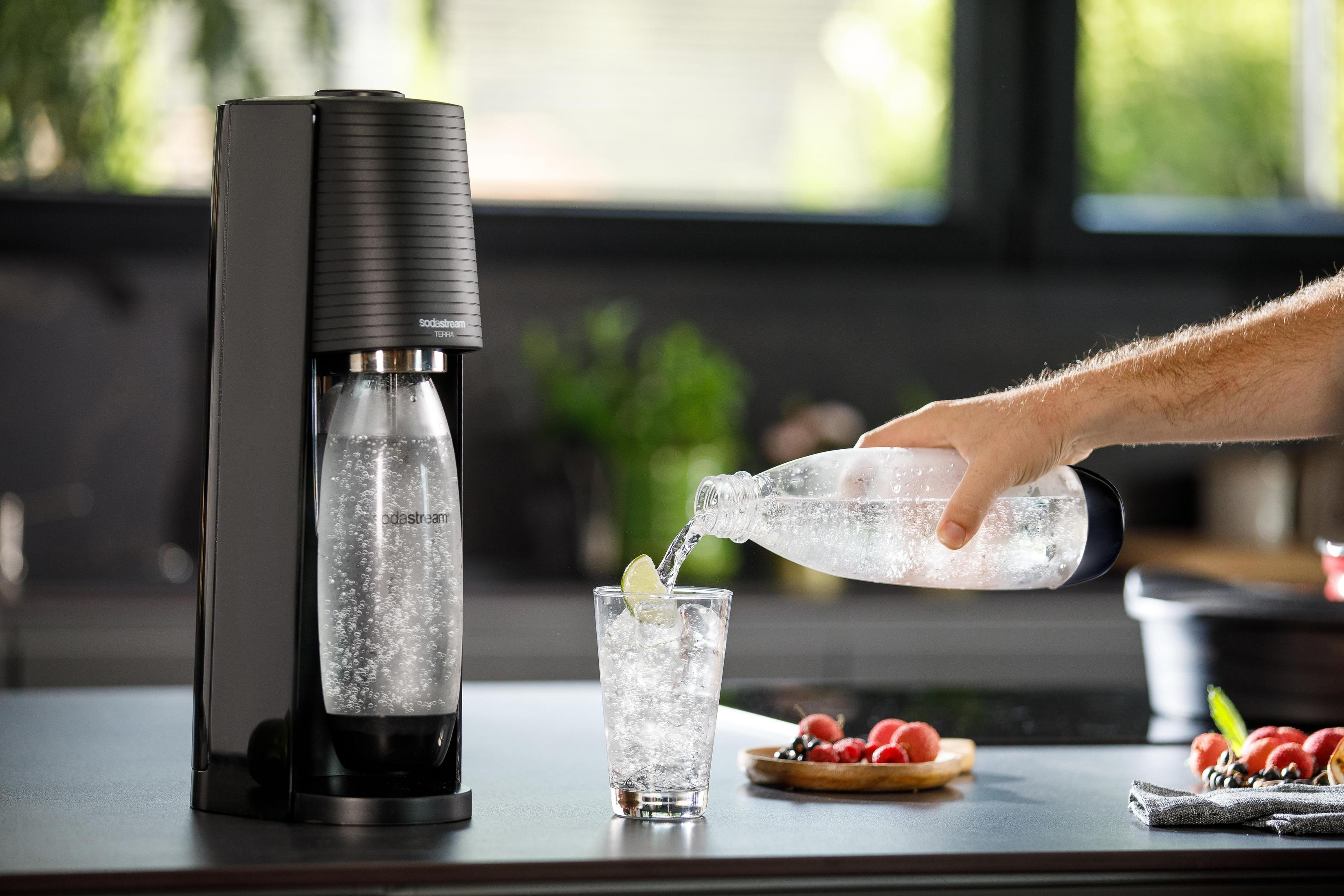 Czarny ekspres SodaStream ze szklanką sody i osobą nalewającą wodę.