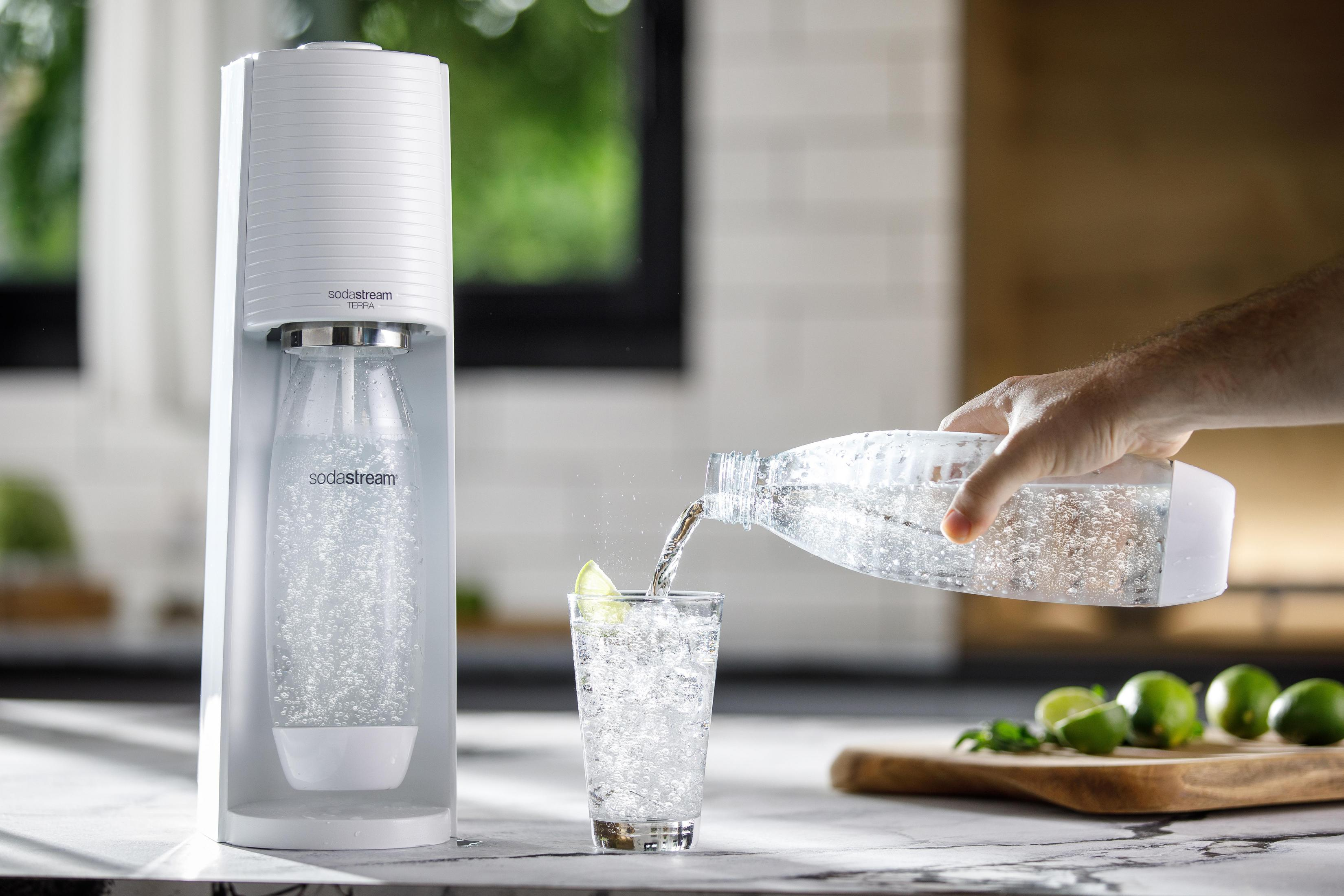 Een persoon giet water uit een soda stream fles in een glas met limoen.