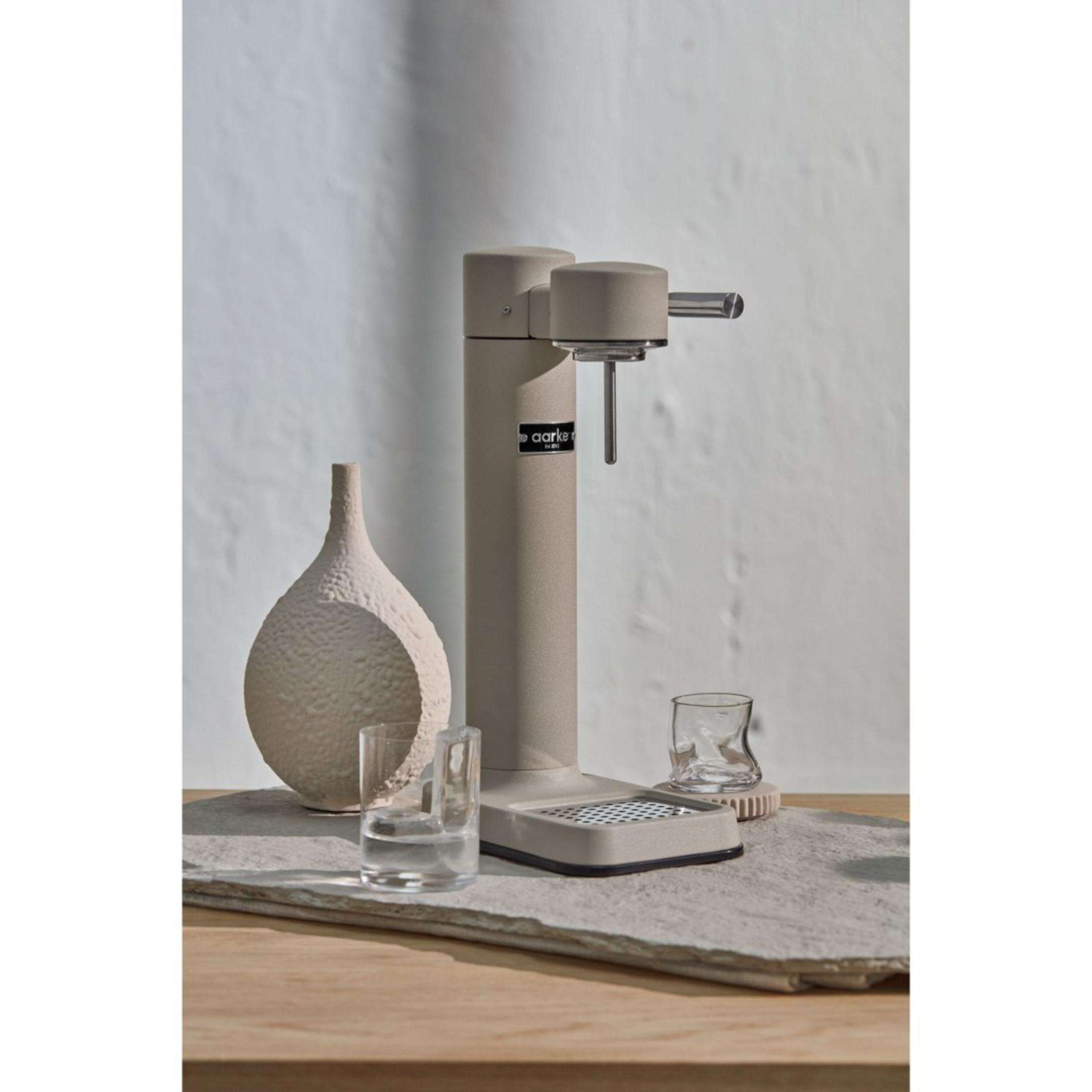 Sodastream beige con bicchieri e un vaso su un tavolo di legno. Sfondo bianco.
