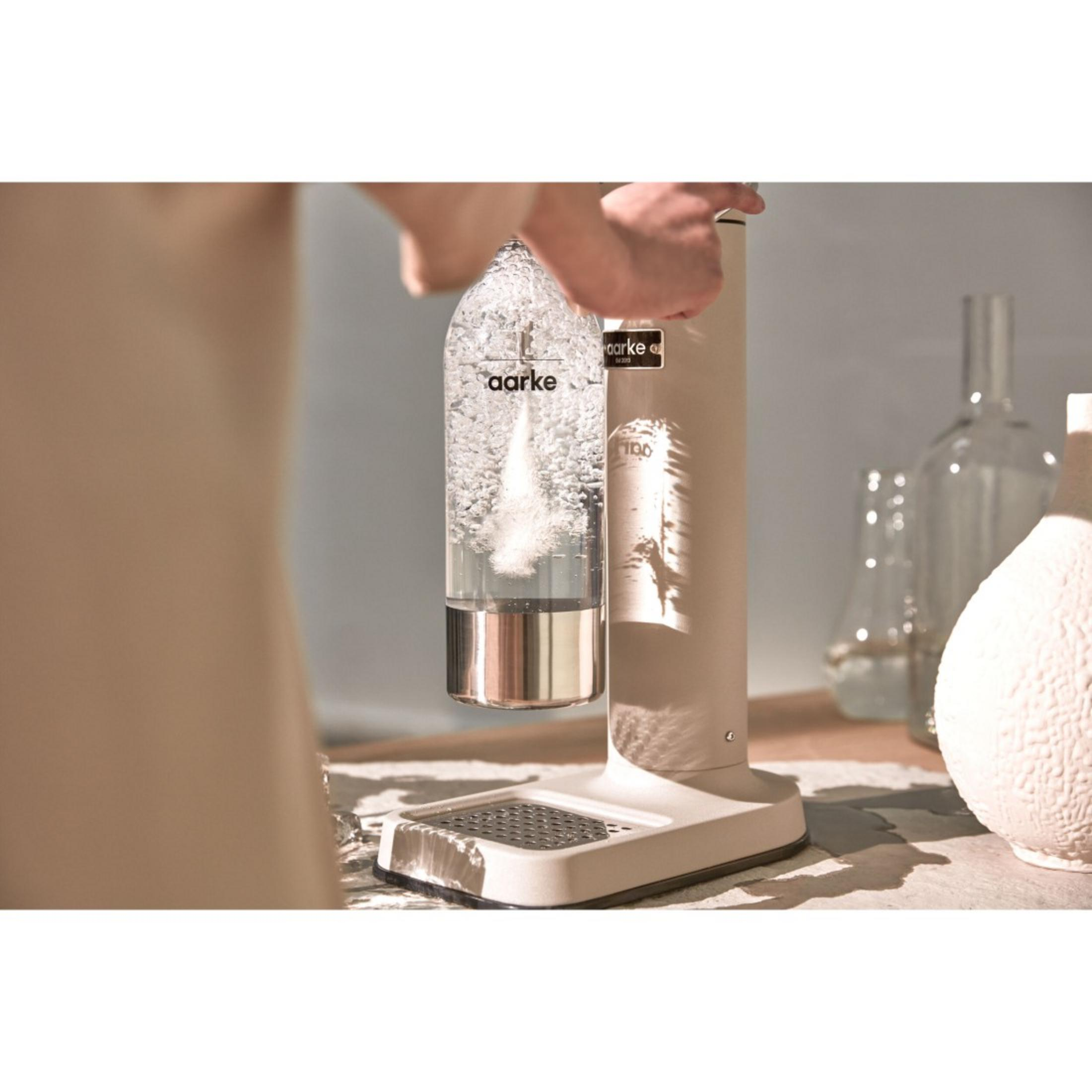 Persona usa un gasatore, acqua si carbonata. Bottiglia trasparente, macchina beige.