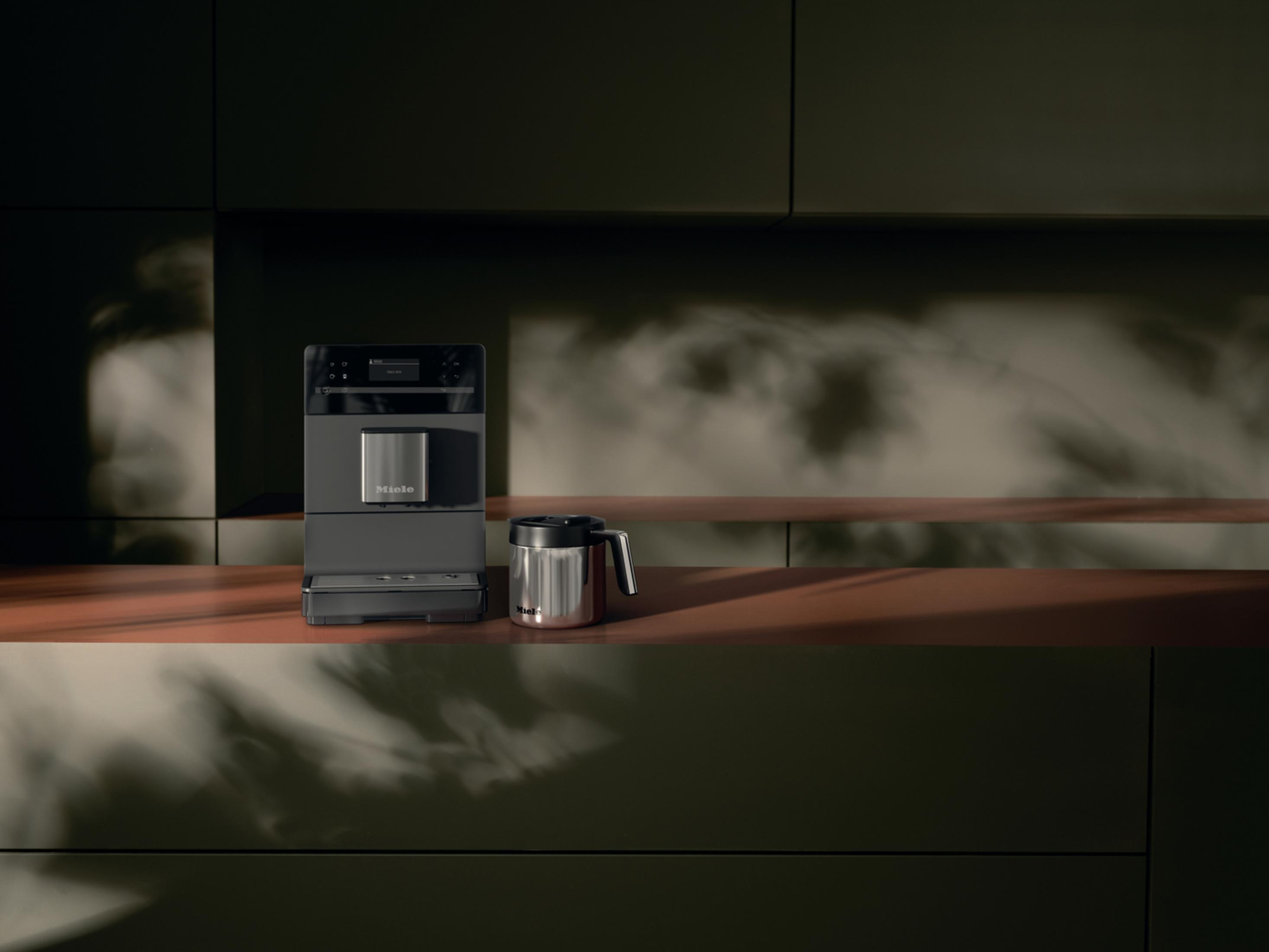 Moderne Kaffeemaschine auf einer Arbeitsplatte, mit einer Edelstahlkaraffe daneben.