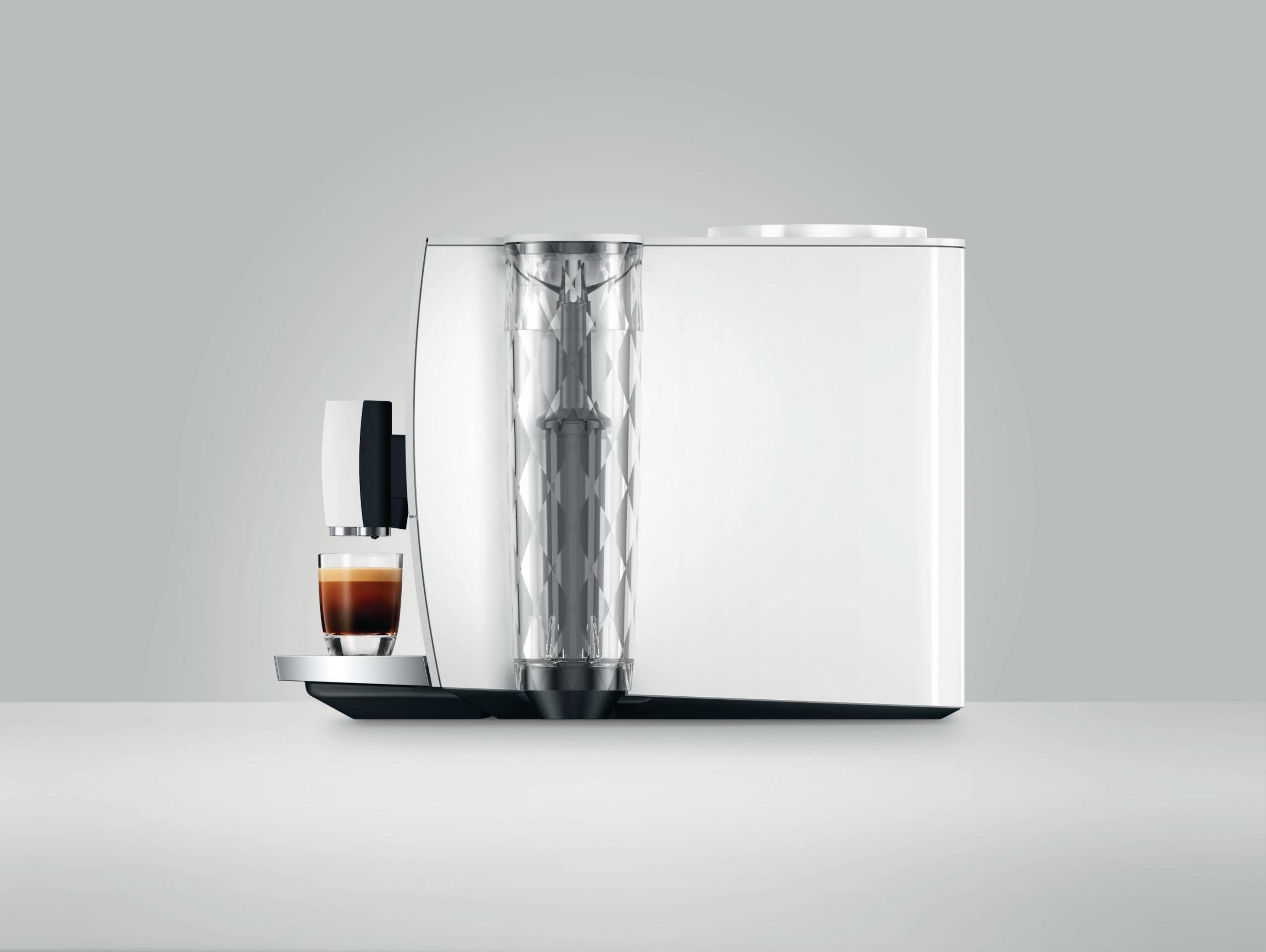 Widok z boku białego ekspresu do kawy ze szklanką kawy.