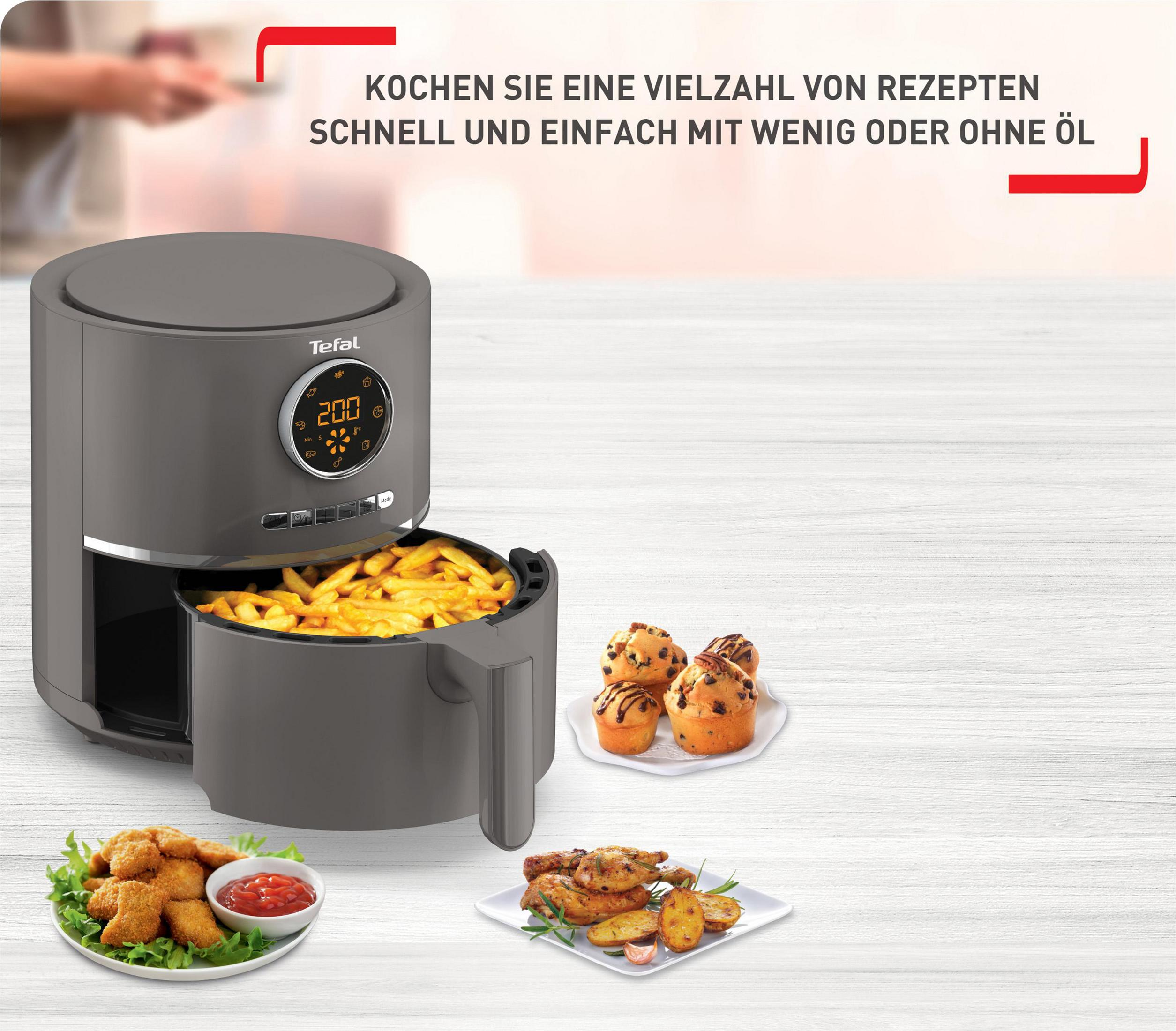 Szara frytownica powietrzna z frytkami i babeczkami na stole z różnymi produktami spożywczymi.