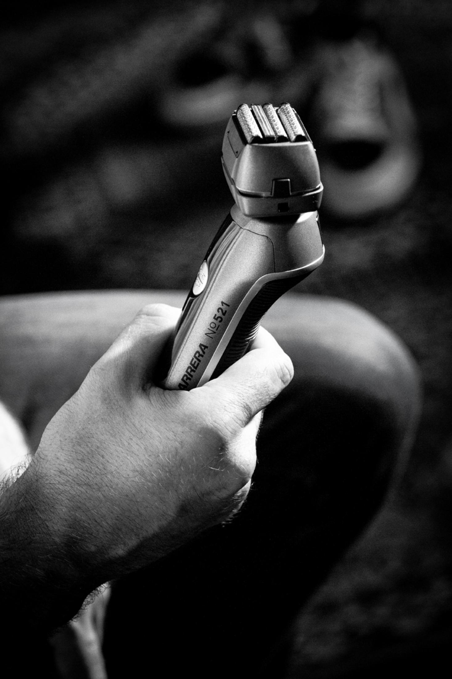 Close-up van een hand die een zwart-zilveren elektrisch scheerapparaat vasthoudt.