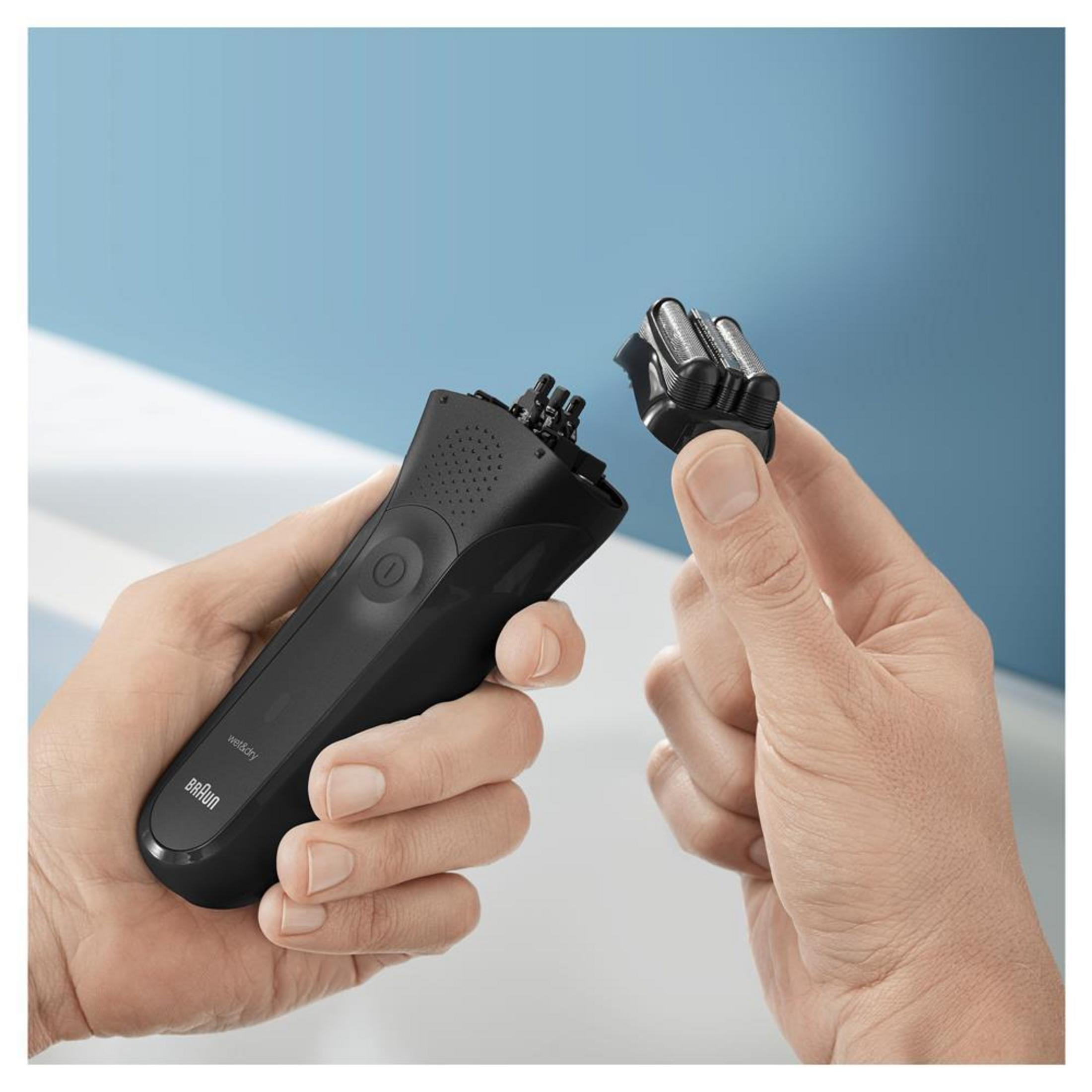 Dłonie trzymają czarną golarkę elektryczną Braun i odłączoną głowicę. Niebieskie tło.