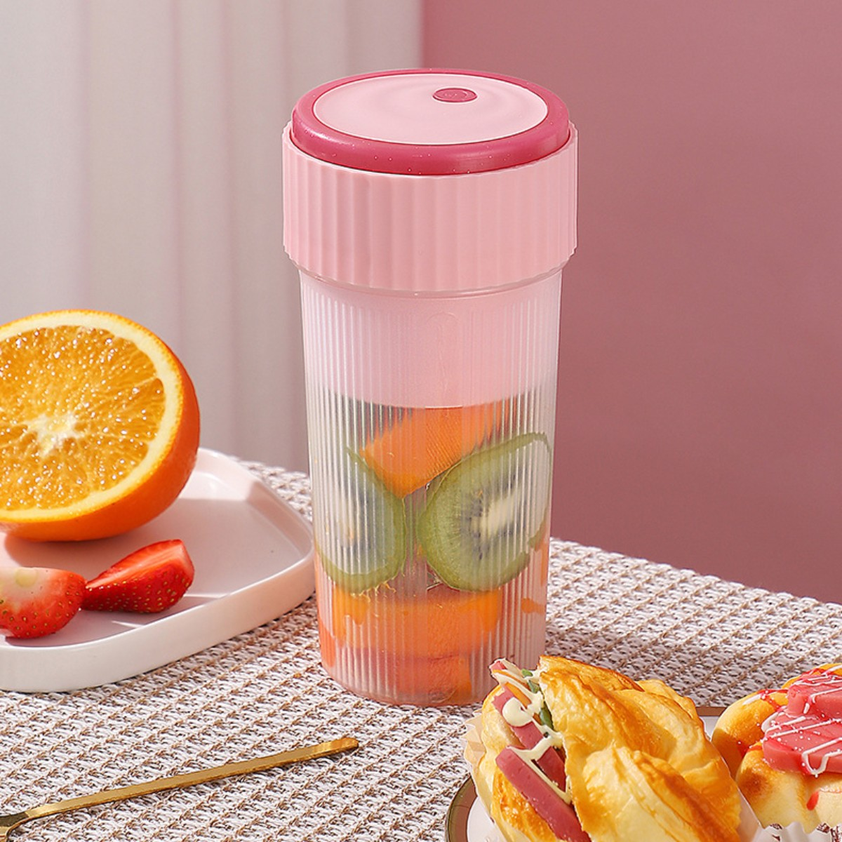 Rosa Mixer mit Früchten. Orangen- und Erdbeerscheiben. Gebäck im Vordergrund.