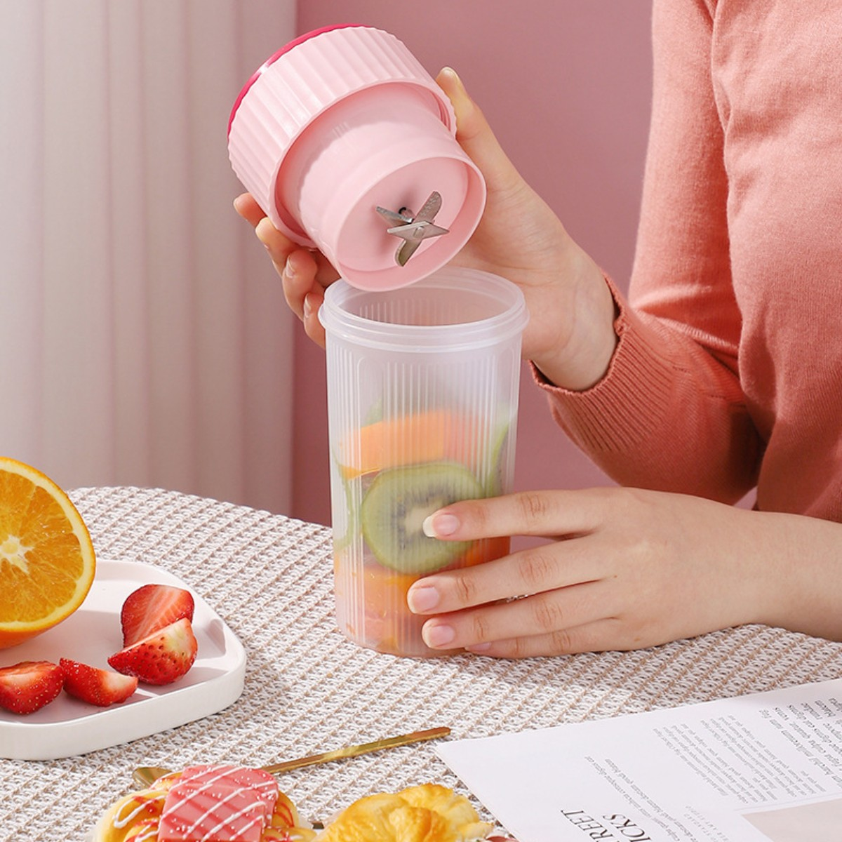 Eine Person setzt einen kleinen rosa Mixer zusammen, in dem sich Früchte in einem transparenten Becher befinden.