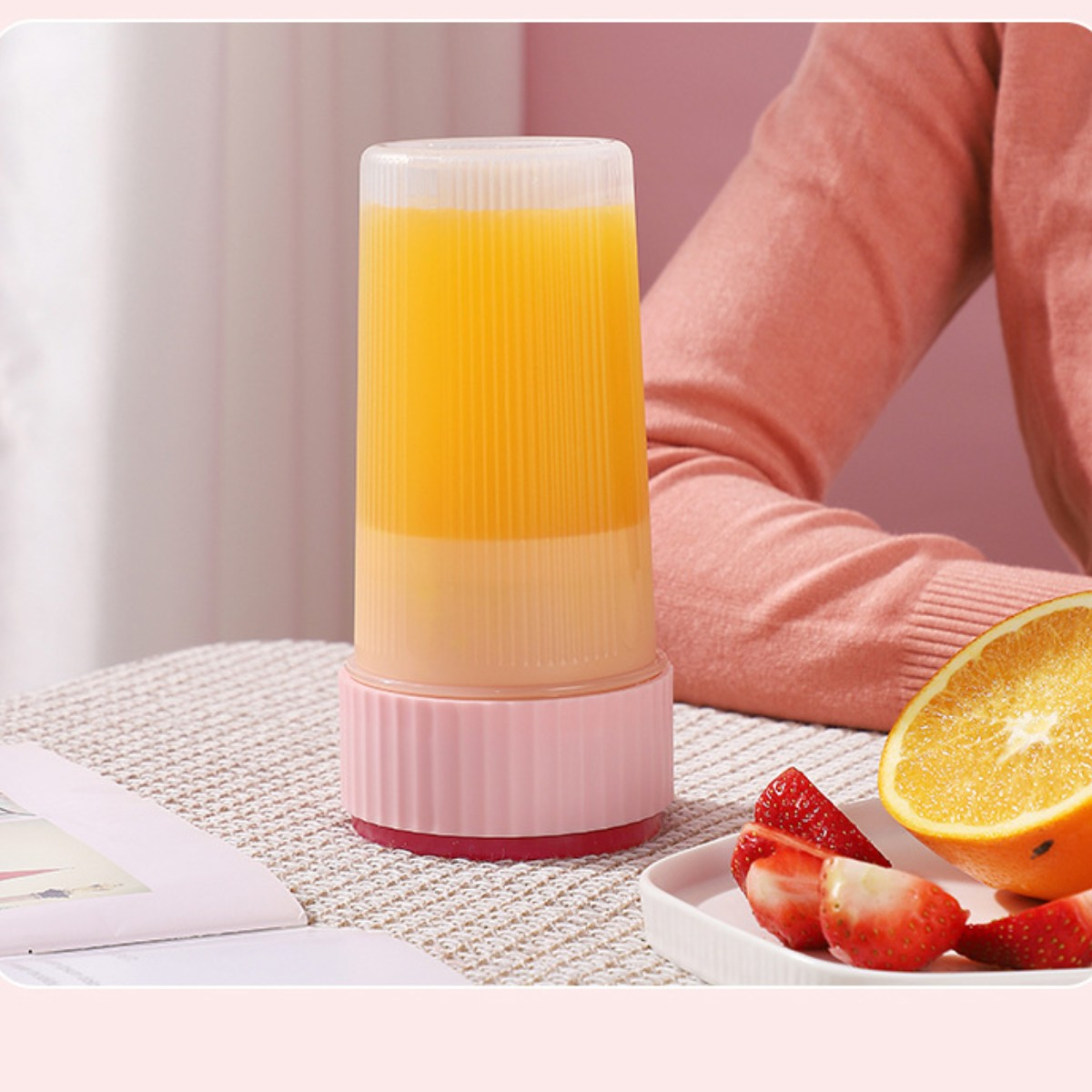 Ein klarer Mixerbecher mit Orangensaft. Aufgeschnittene Erdbeeren und eine halbe Orange auf einem Teller.
