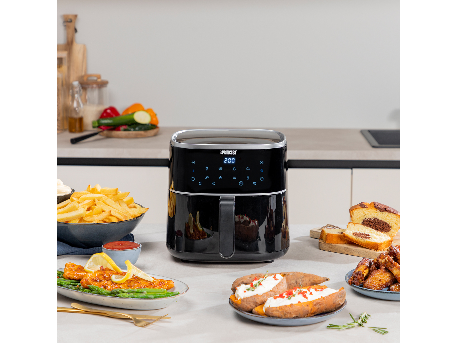 Czarna frytkownica na stole z jedzeniem, pokazująca wyświetlacz i jedzenie wokół niej.