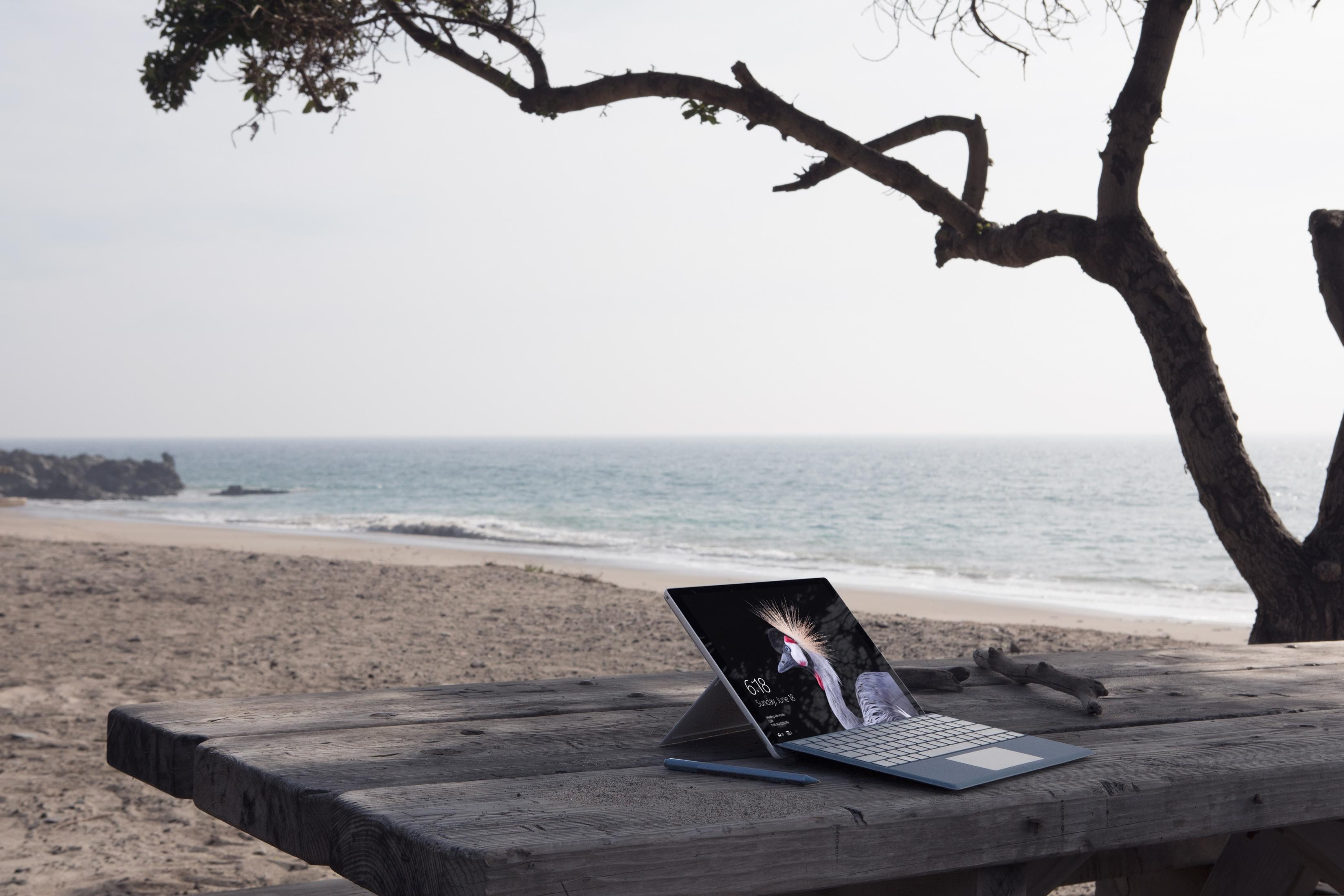 Laptop auf einem Holztisch mit Strand, Baum und Ozean im Hintergrund.