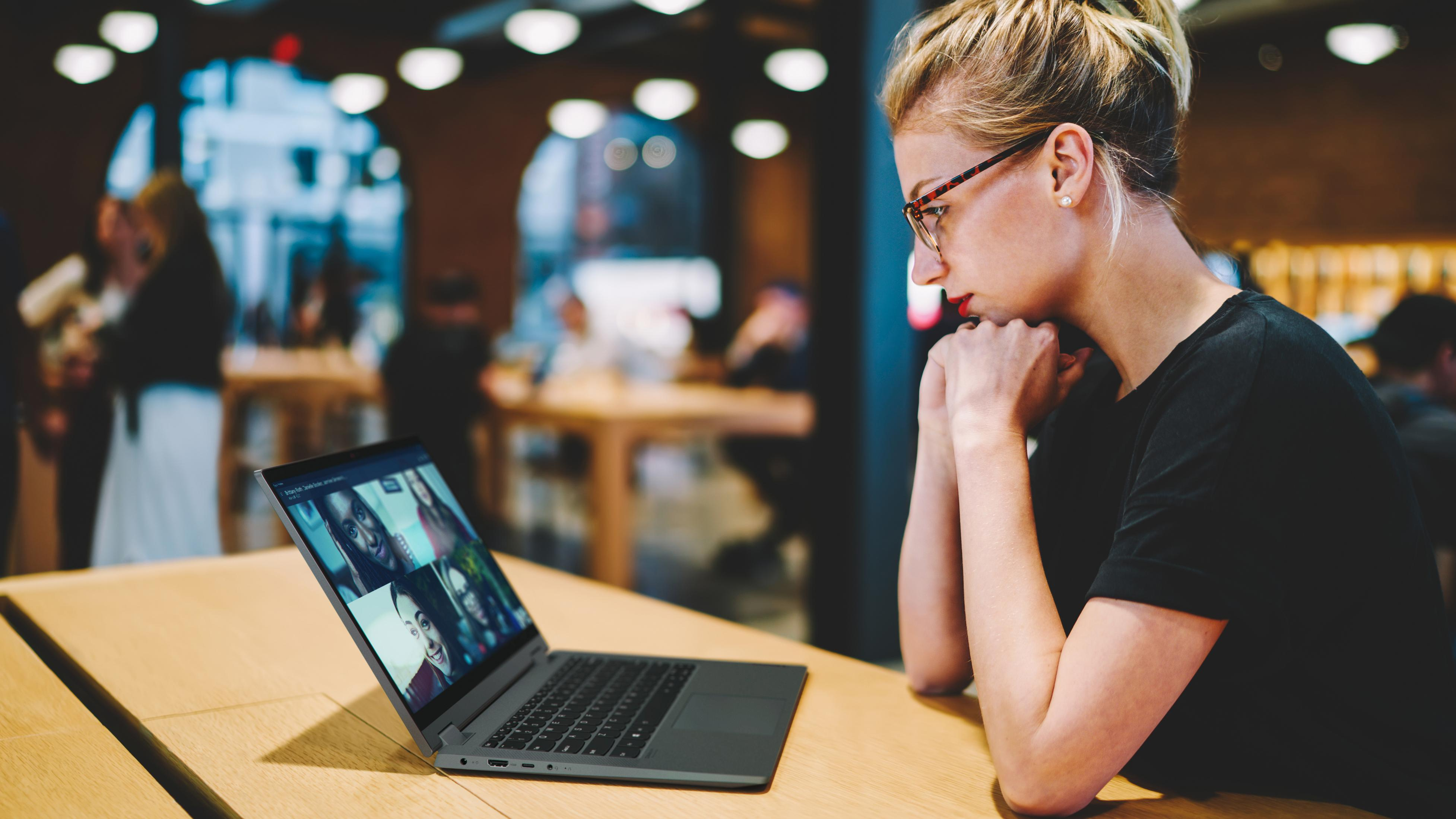 Eine Frau mit Brille schaut auf einen Laptop-Bildschirm, der einen Videoanruf zeigt.