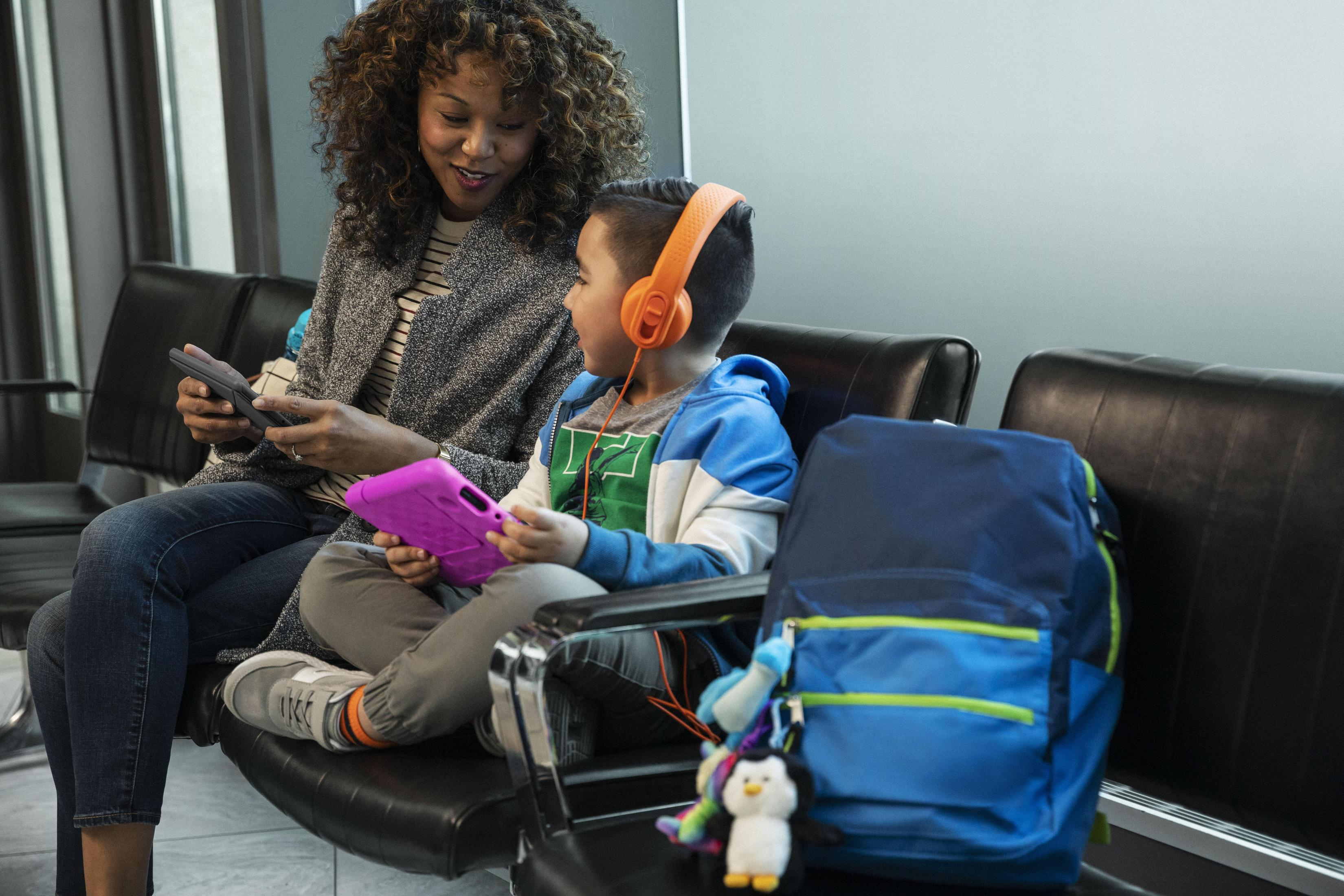Eine Frau und ein Junge sitzen, beide mit einem Tablet. Der Junge trägt Kopfhörer.