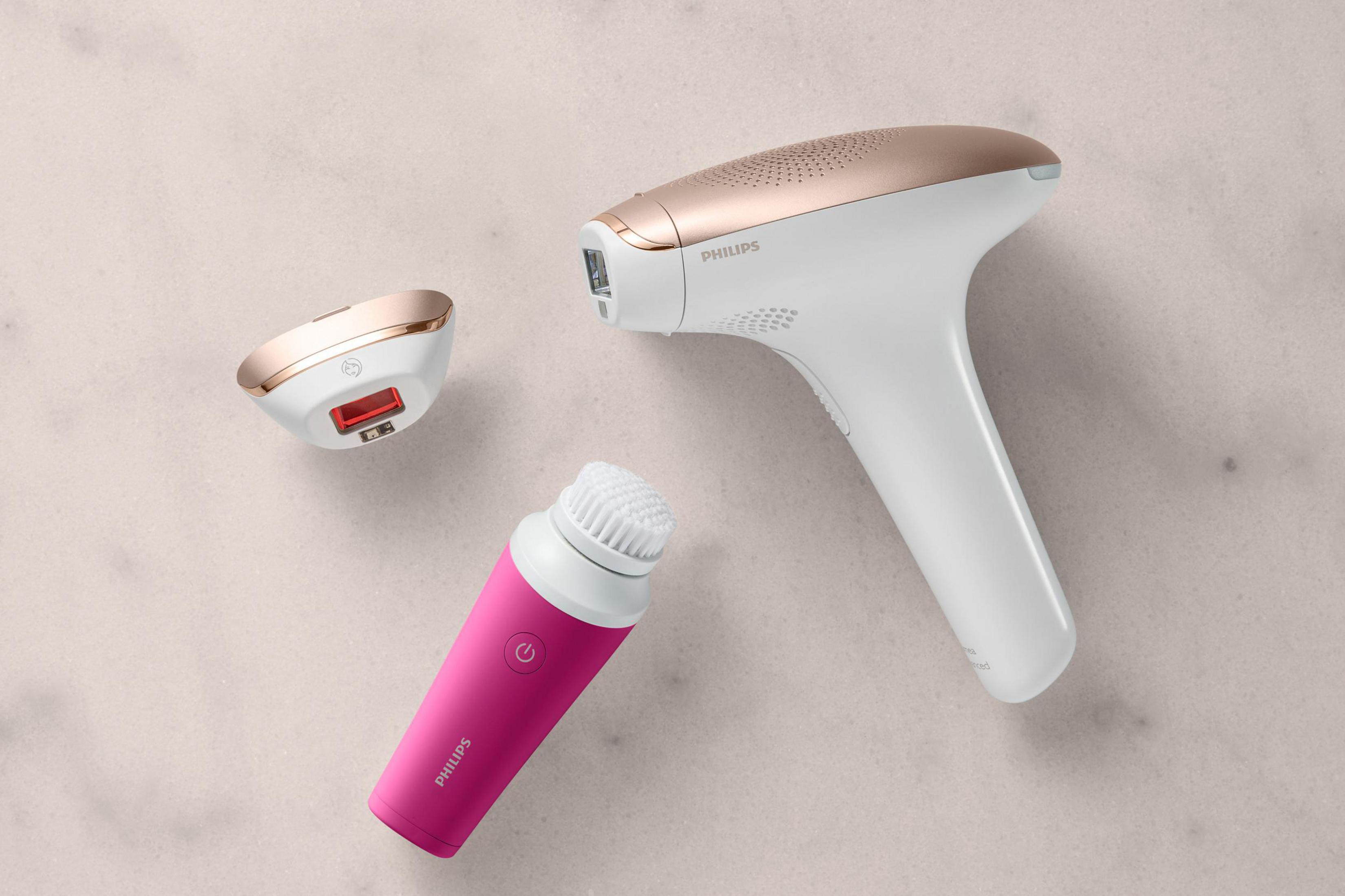 Trzy białe i różowo-złote urządzenia do pielęgnacji Philips na teksturowanej powierzchni. Różowa szczotka.
