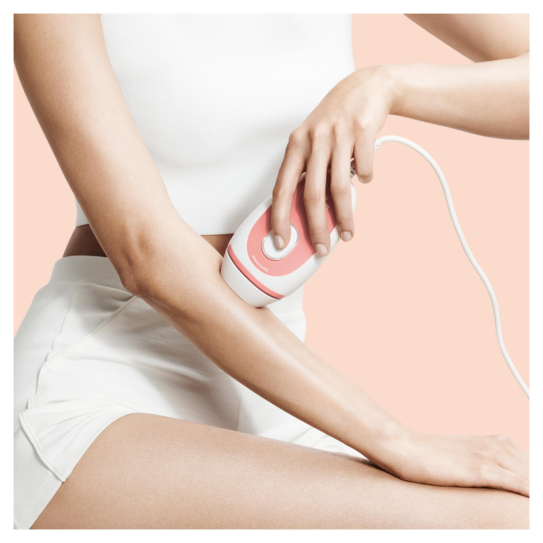 Osoba używa różowo-białego urządzenia do usuwania włosów na ramieniu.
