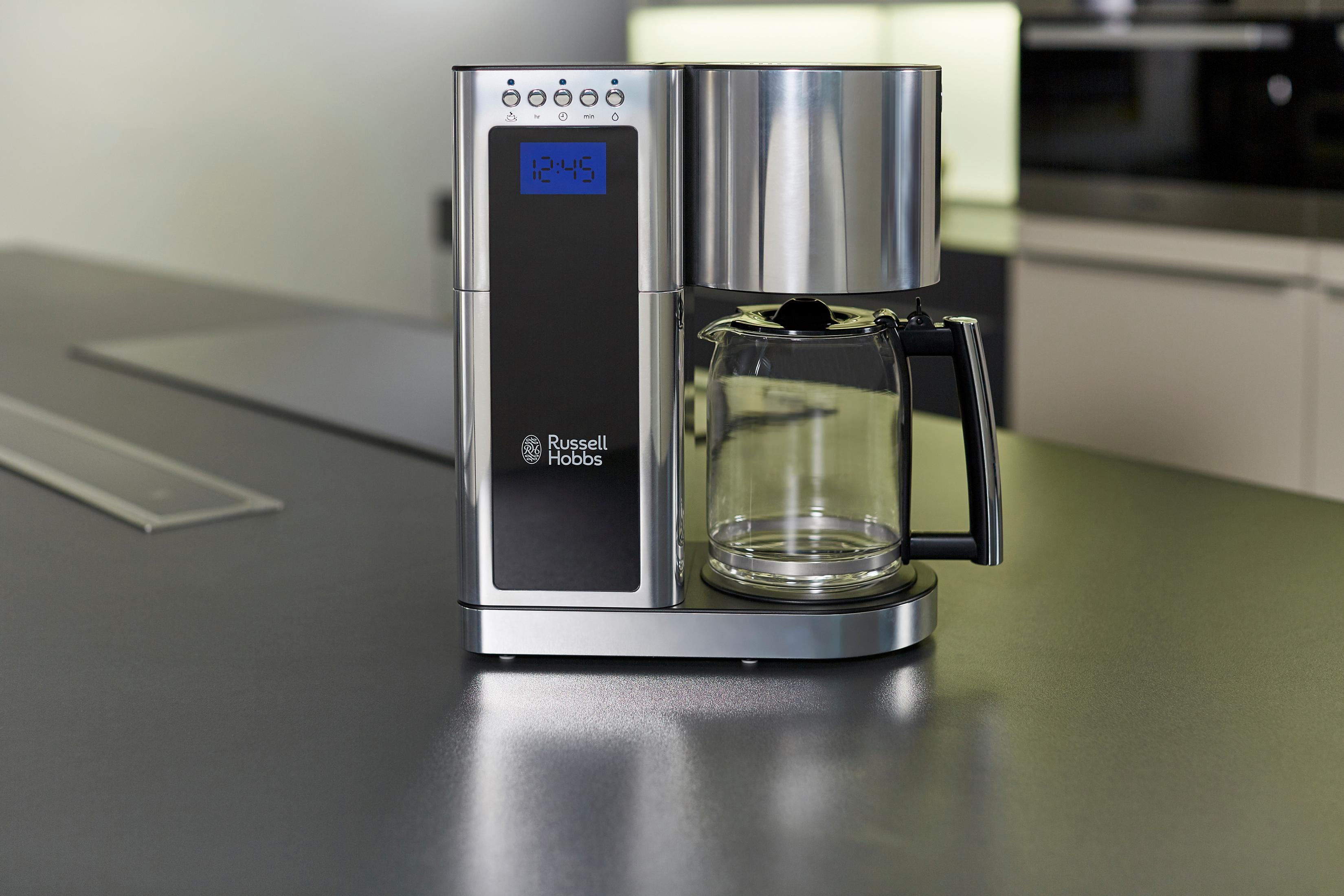 Una caffettiera in acciaio inossidabile con una caraffa in vetro su un piano di lavoro scuro.
