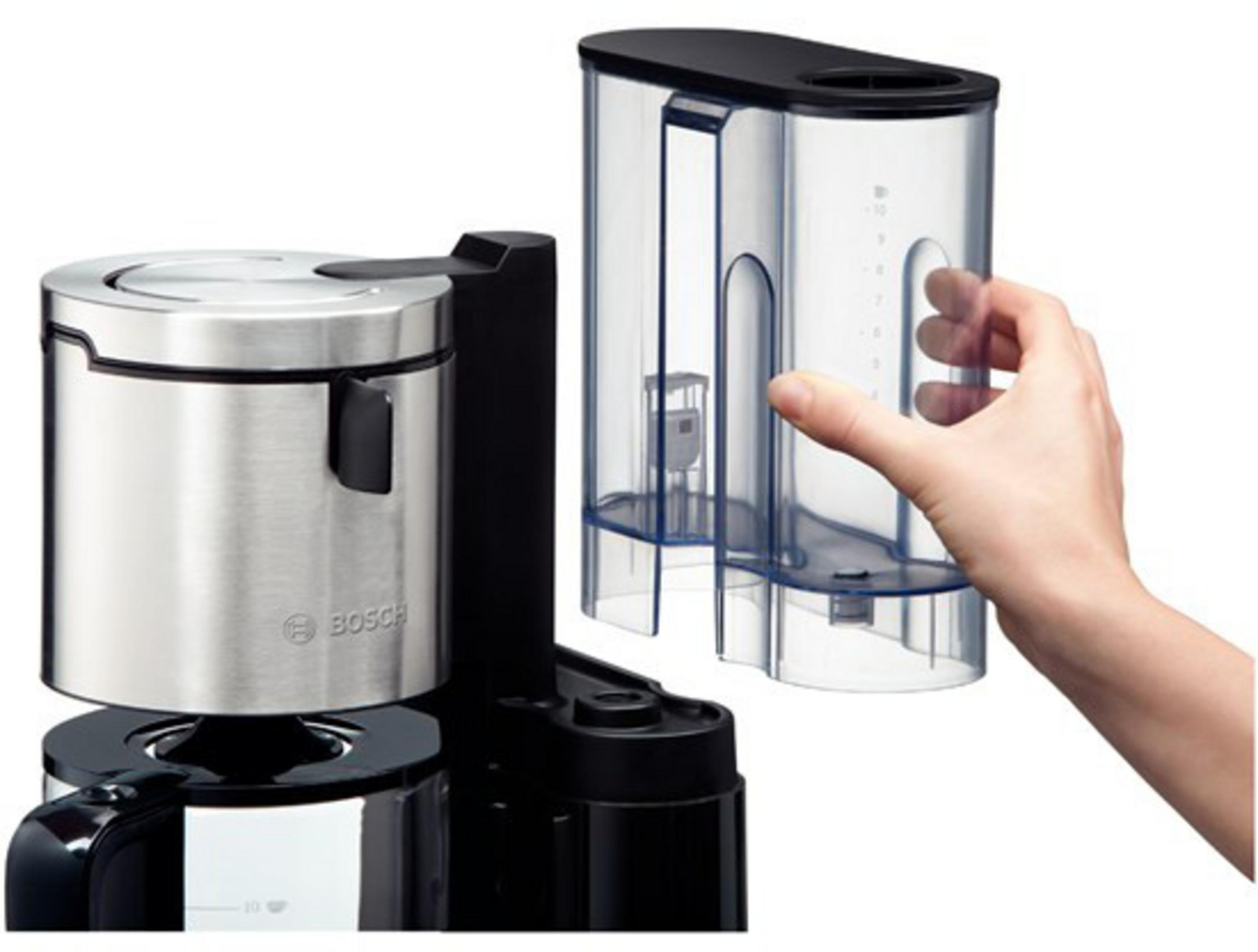 Ekspres do kawy ze srebrnym pojemnikiem i przezroczystym zbiornikiem na wodę. Ręka trzyma zbiornik.