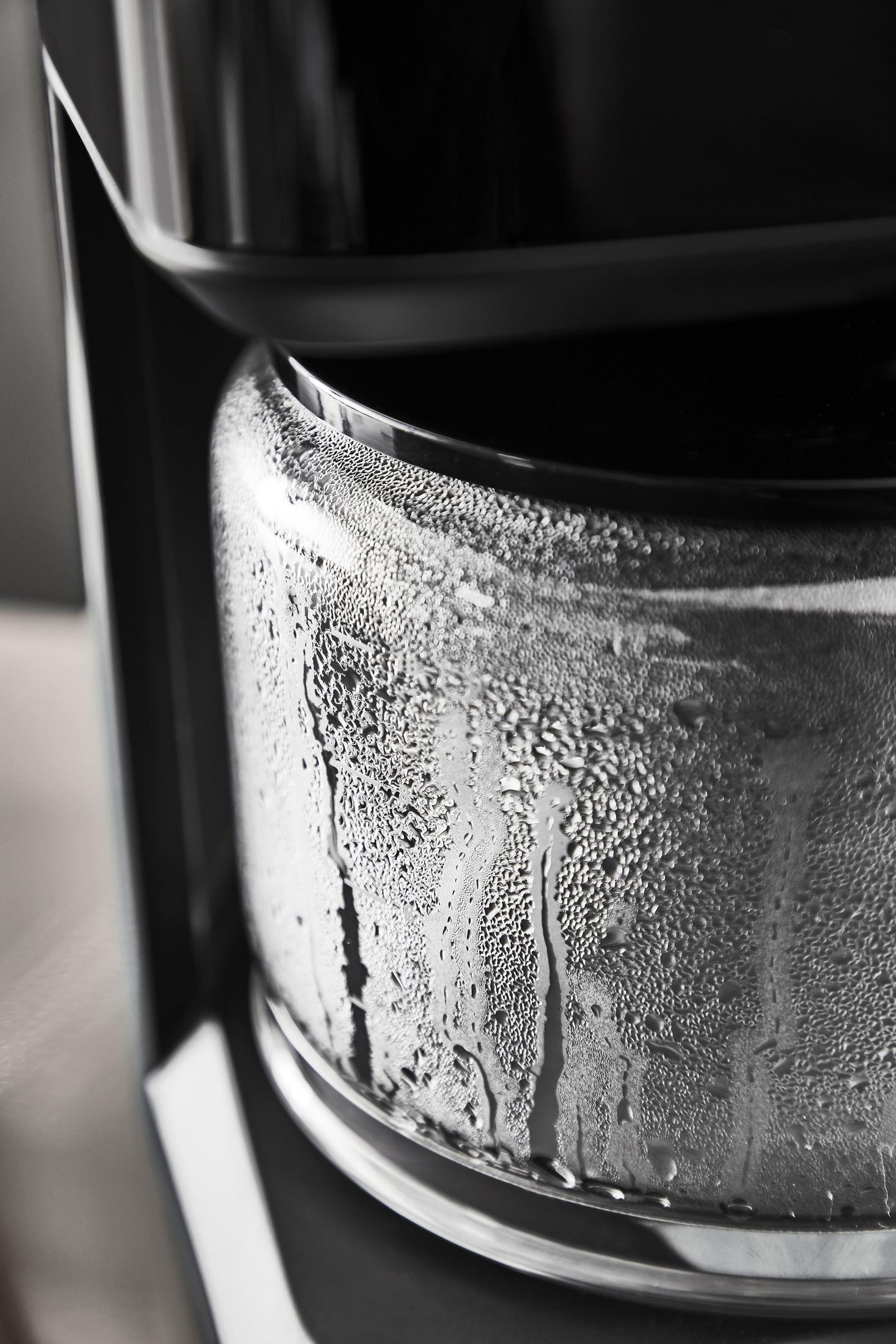 Zbliżenie szklanego dzbanka do kawy z kondensacją wody i czarną pokrywą.