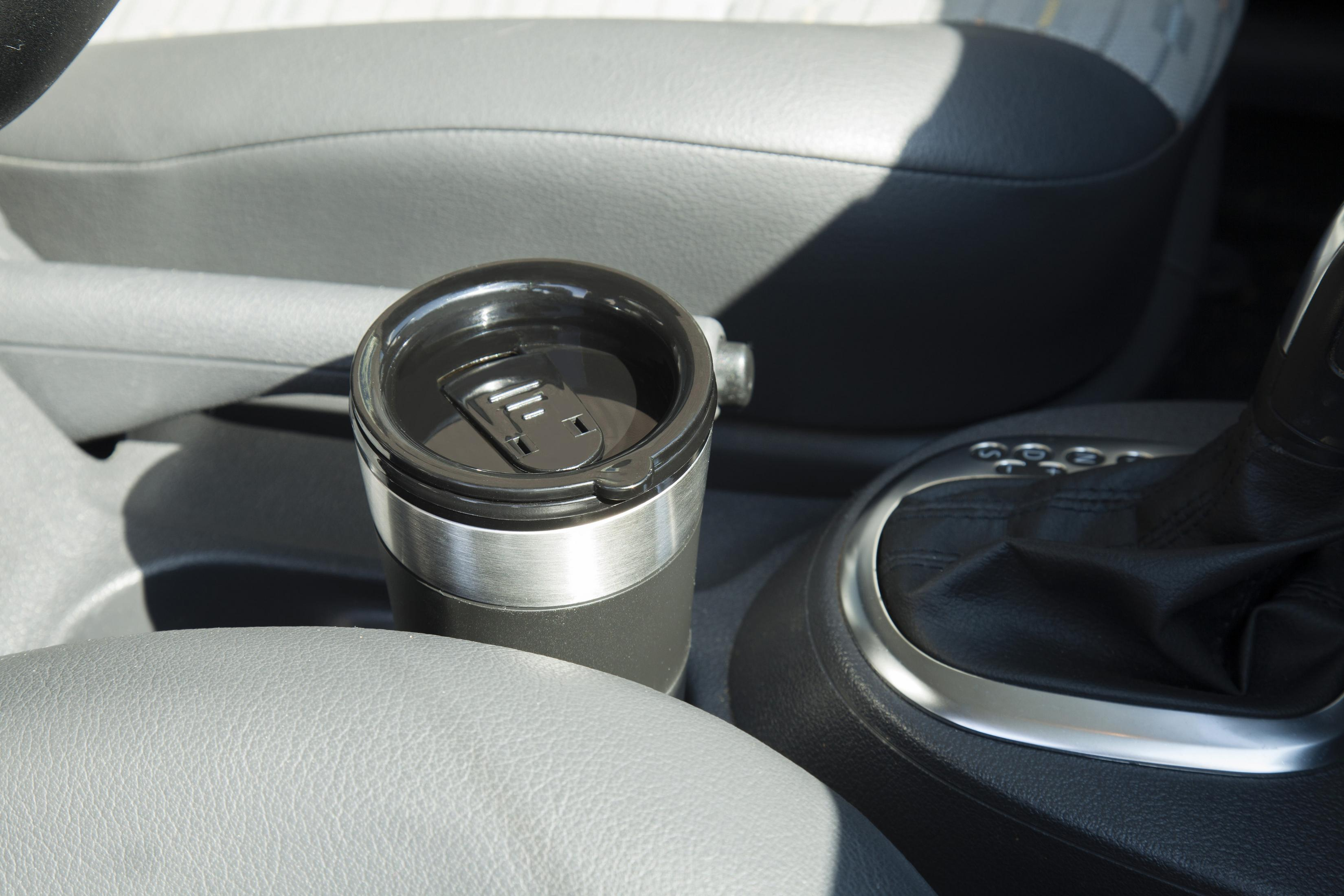 Czarny i srebrny kubek podróżny w uchwycie na kubek samochodowy, z szarym wnętrzem.
