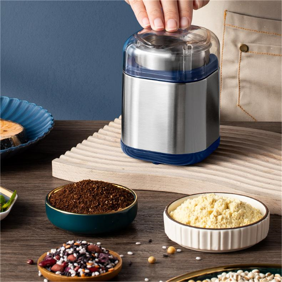 Ein silber-blauer elektrischer Grinder mit Kaffeepulver und Gewürzen in Schalen.