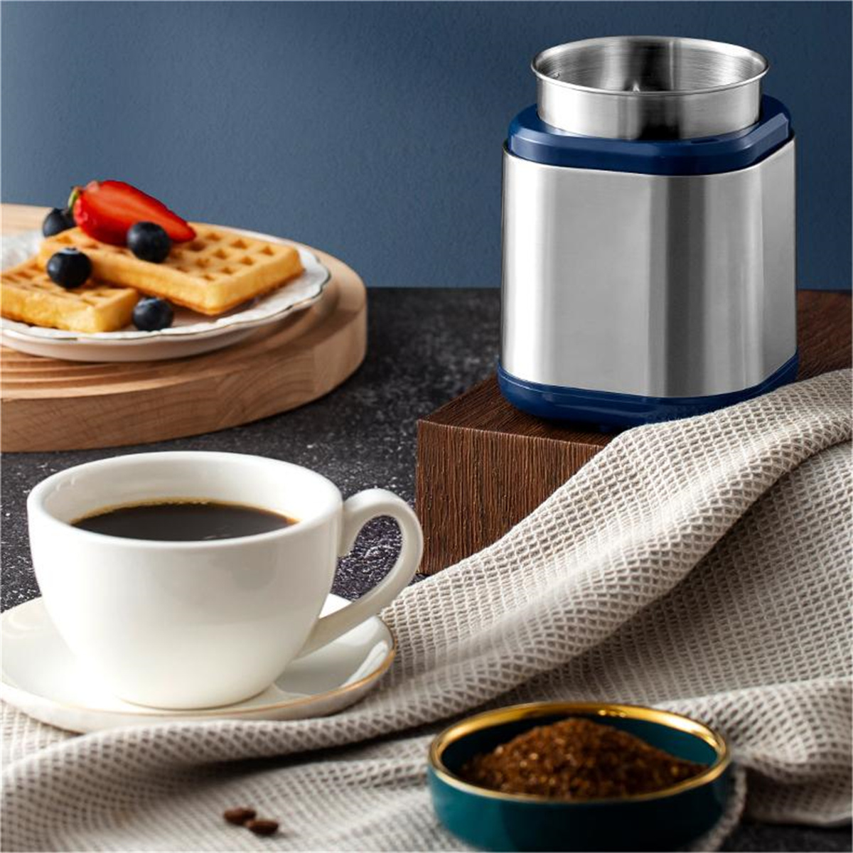 Kaffeetasse, Waffeln mit Beeren und Kaffeemühle auf einem Tisch. Dunkelblauer und weißer Hintergrund.