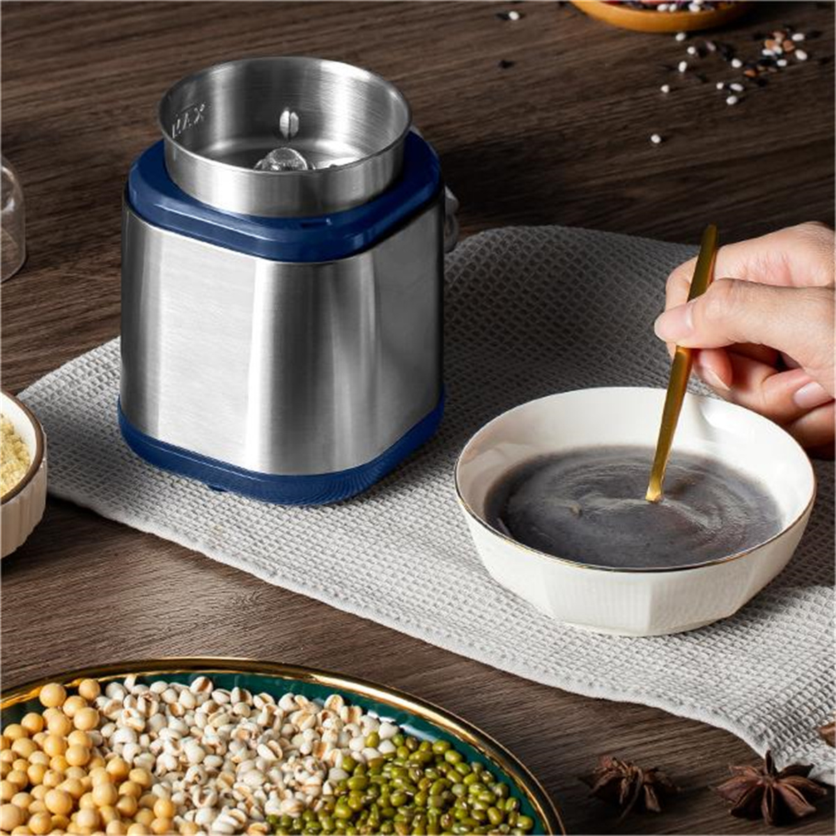 Eine Küchenmaschine mit blauem Sockel, neben einer Schüssel mit schwarzer Sesampaste und Zutaten.