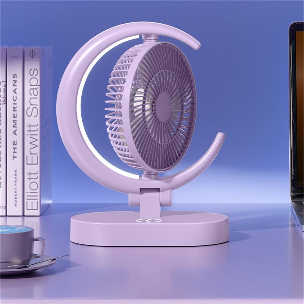 Ein moderner, hellvioletter Ventilator mit halbmondförmigem Rahmen und kleinem Sockel auf einem Schreibtisch.