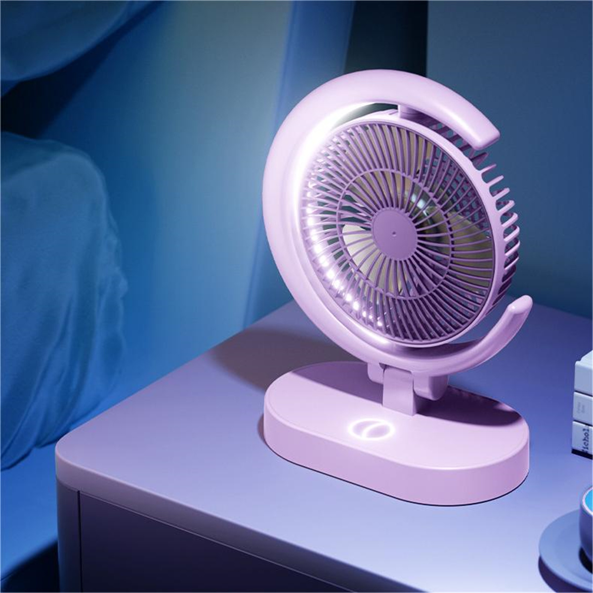 Ein rosa Ventilator mit kreisförmigem Licht. Er steht auf einem lila Tisch. Wand im Hintergrund.