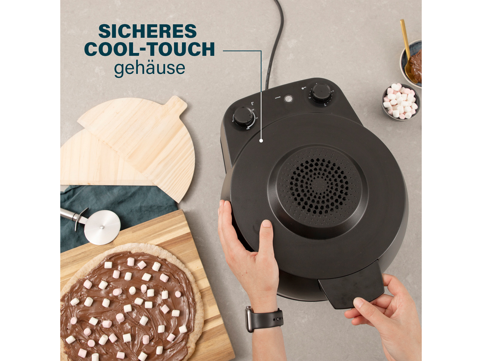 Aparato negro con base de pizza y malvaviscos. El texto dice 'Sicheres Cool-Touch Gehäuse'.