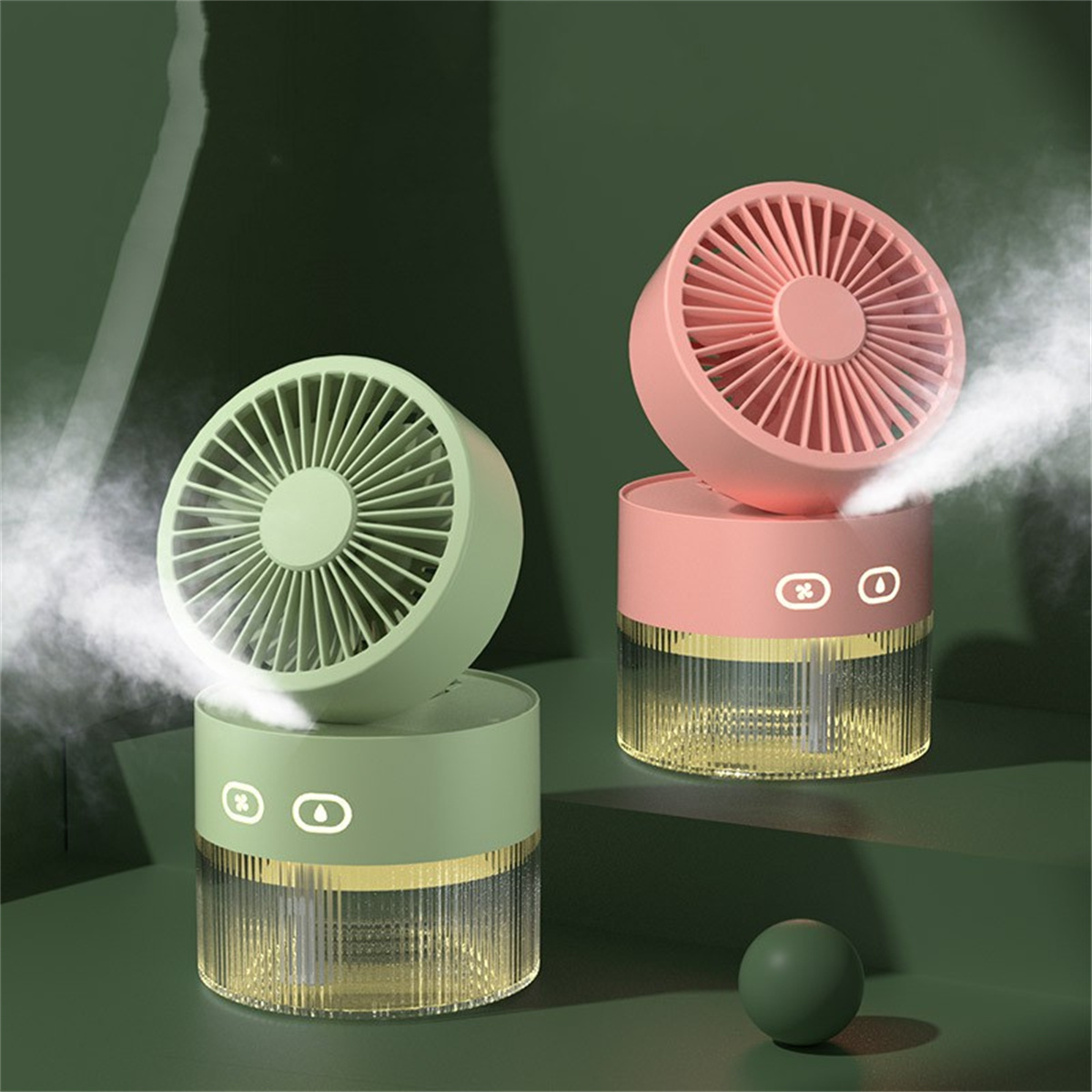 Zwei kleine, bunte Ventilatoren mit Nebel, grün und rosa, auf einer dunkelgrünen Oberfläche.