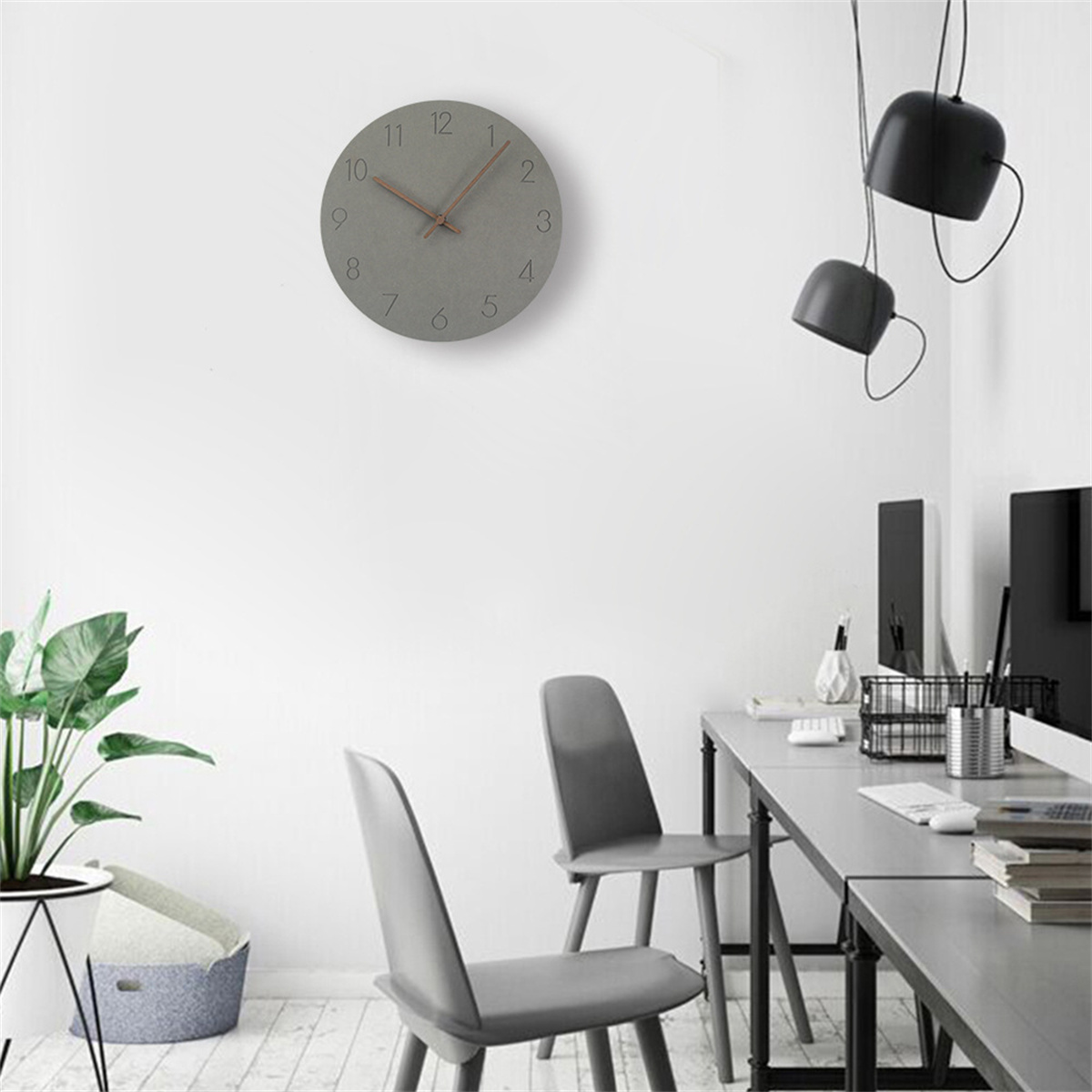 Graue runde Uhr an einer weißen Wand. Drei schwarze Pendelleuchten. Graue Stühle und Tisch.
