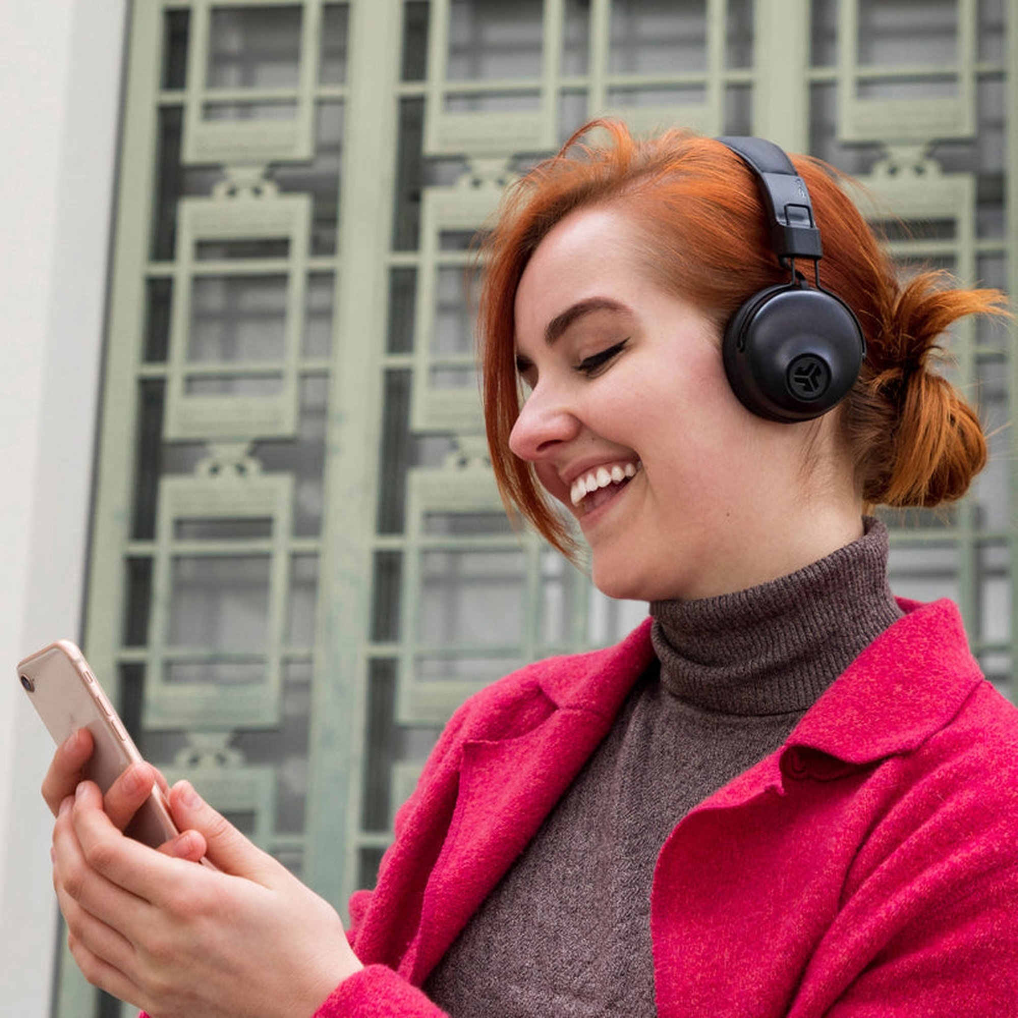 Una mujer con auriculares mirando un teléfono. Ella está sonriendo.