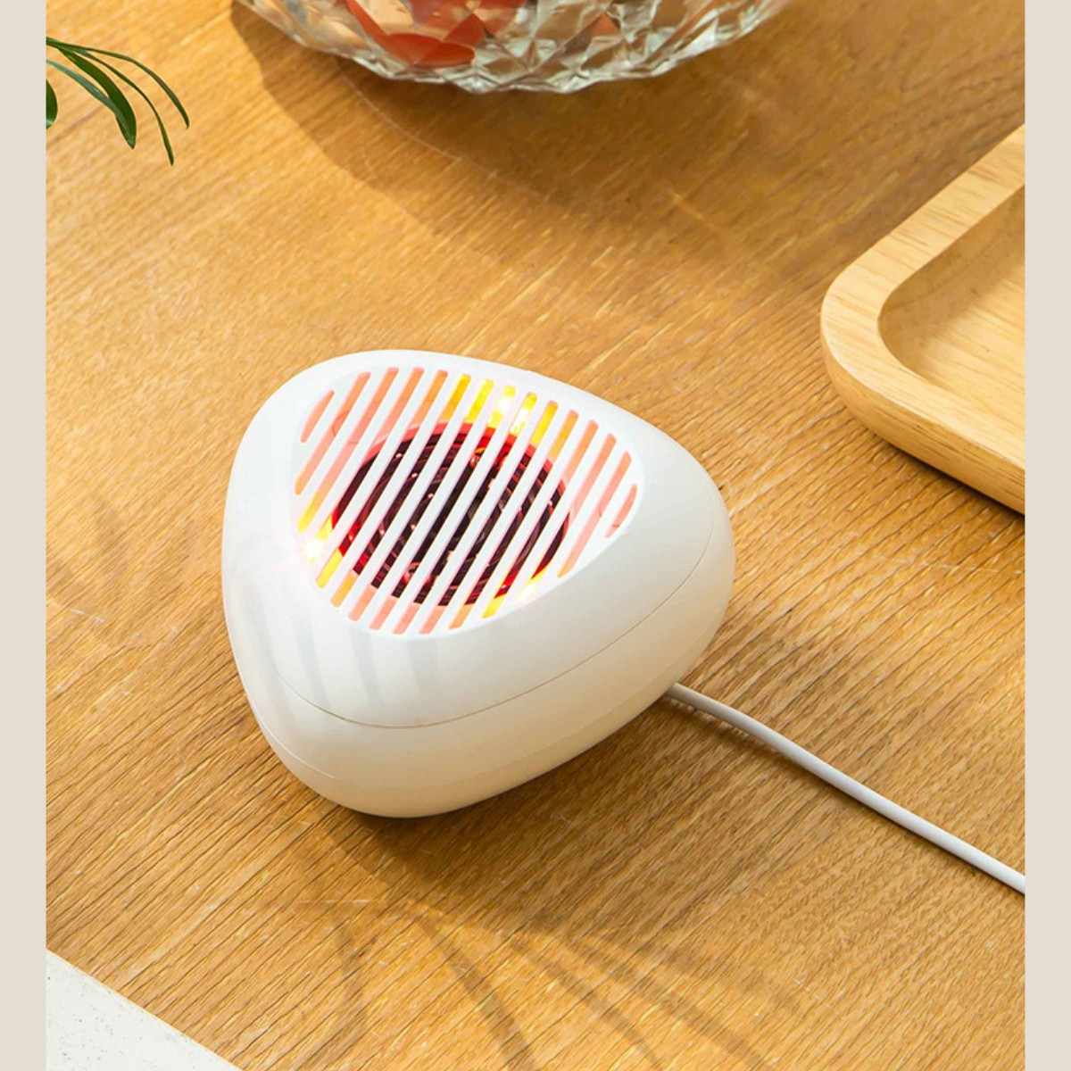 Weißes, dreieckiges Gerät auf Holztisch. Es hat rote und gelbe Lichter und ein weißes Kabel.