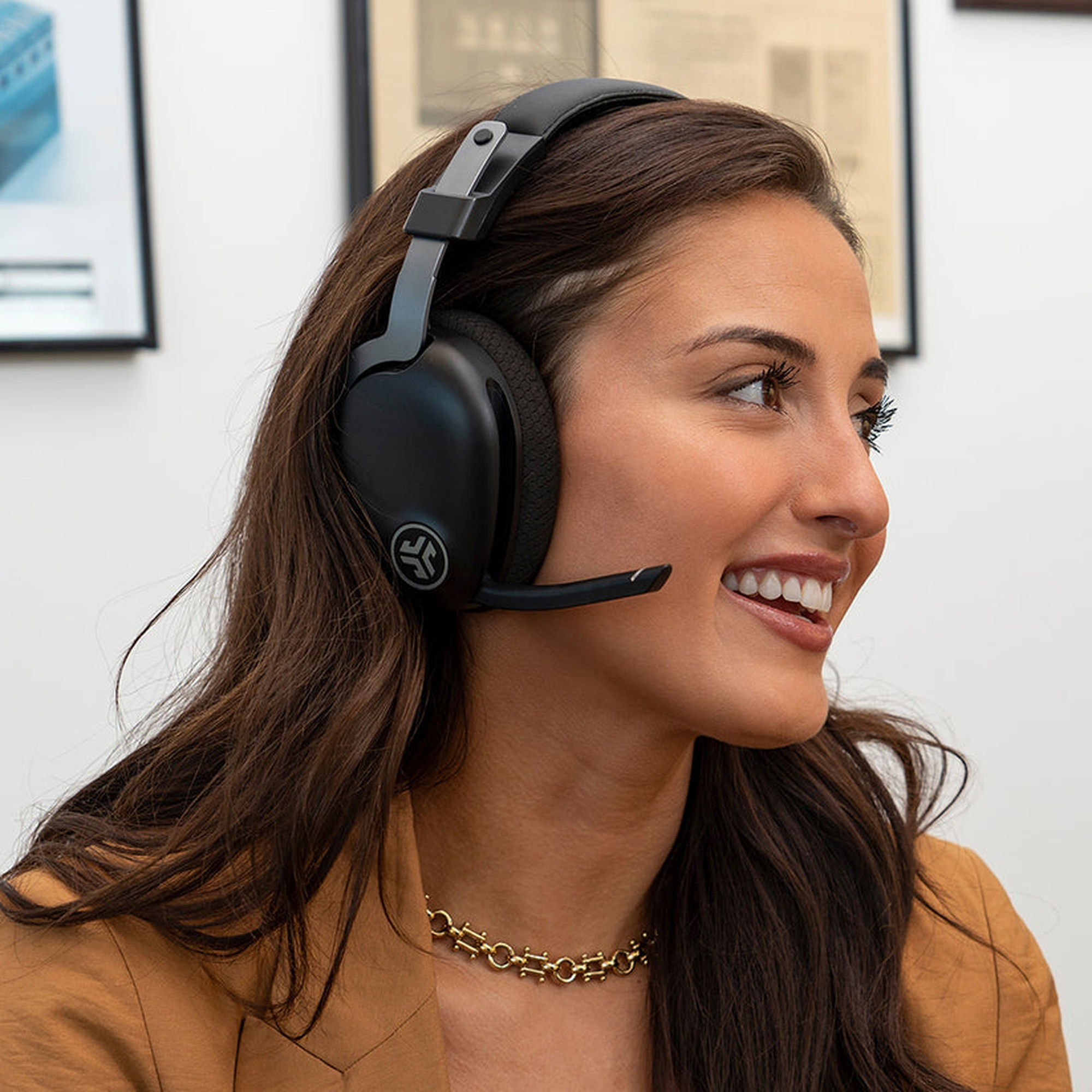 Frau mit schwarzem Headset lächelt, goldene Halskette, brauner Blazer, lächelnd.
