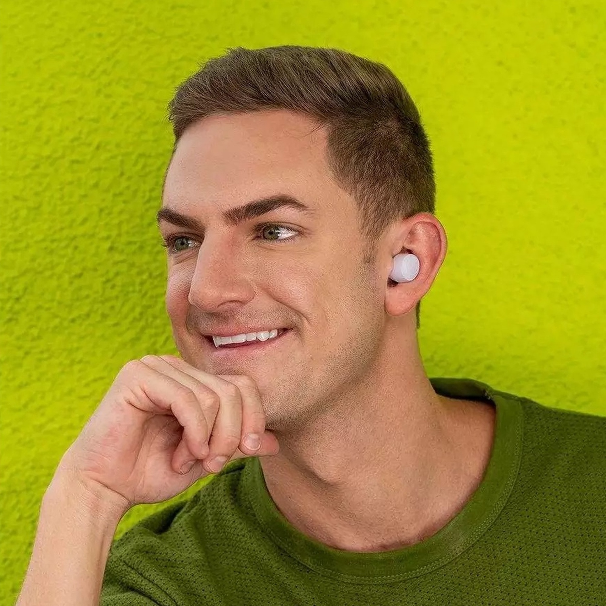 Mężczyzna z wkładką douszną w uchu. Uśmiecha się, ma krótkie włosy.