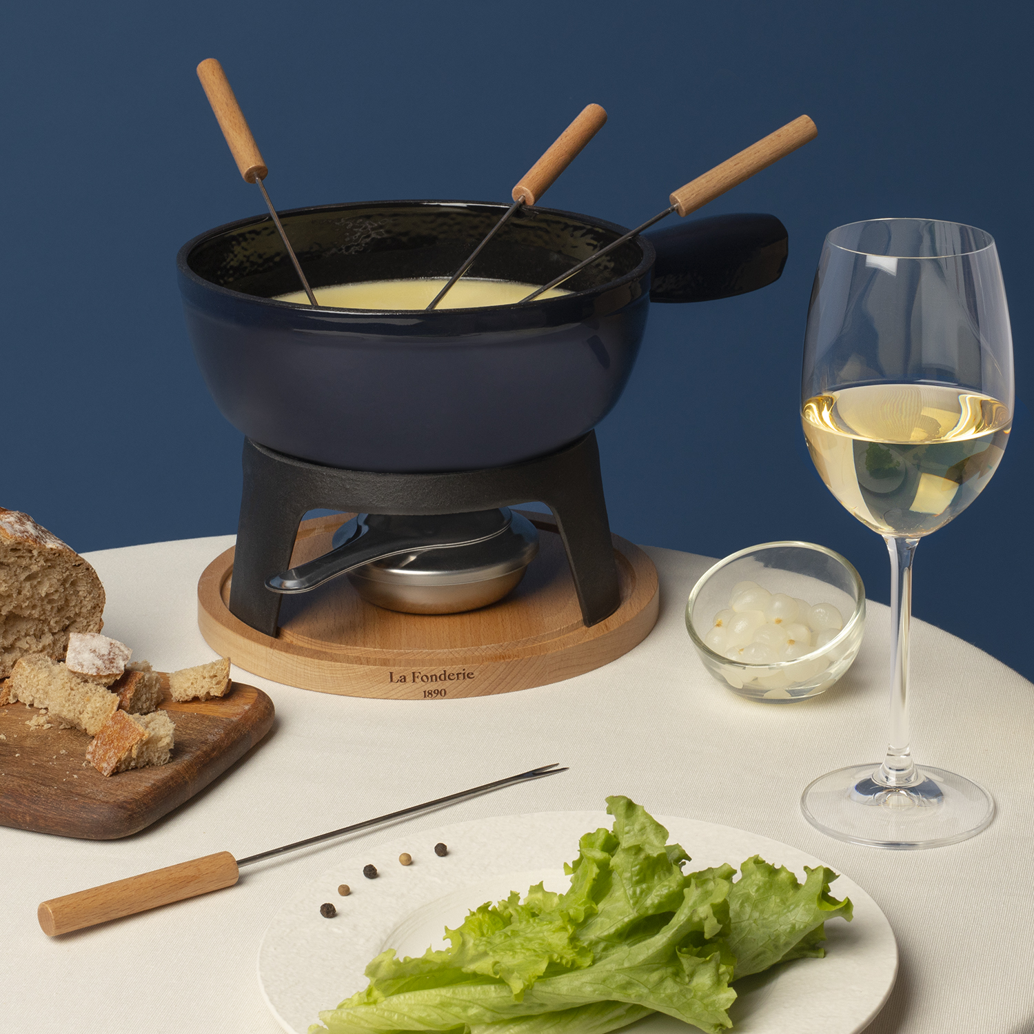 Pentola per fonduta con formaggio, forchette, pane e un bicchiere di vino. Pentola nera su un supporto in legno.