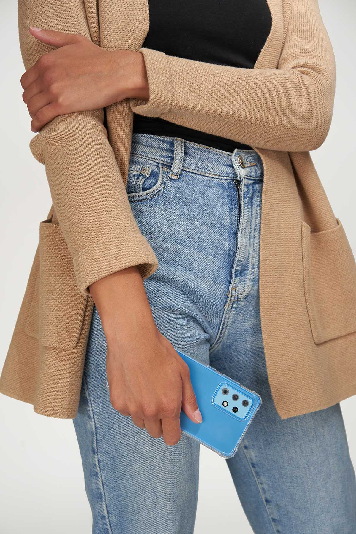 Person hält eine blaue Handyhülle, trägt einen beigen Cardigan und blaue Jeans.