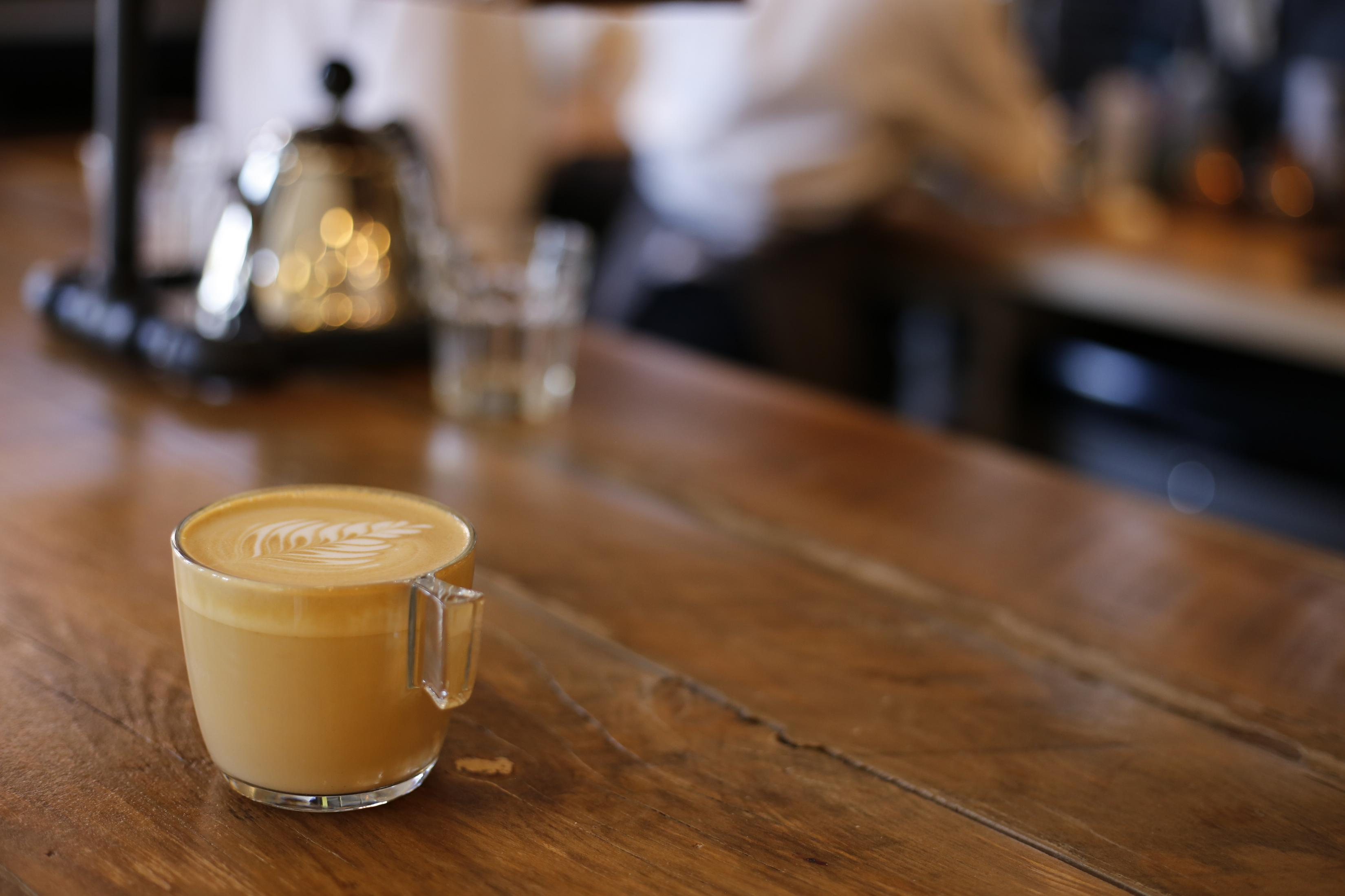 Latte in einer durchsichtigen Tasse mit Henkel, auf einem Holztisch.