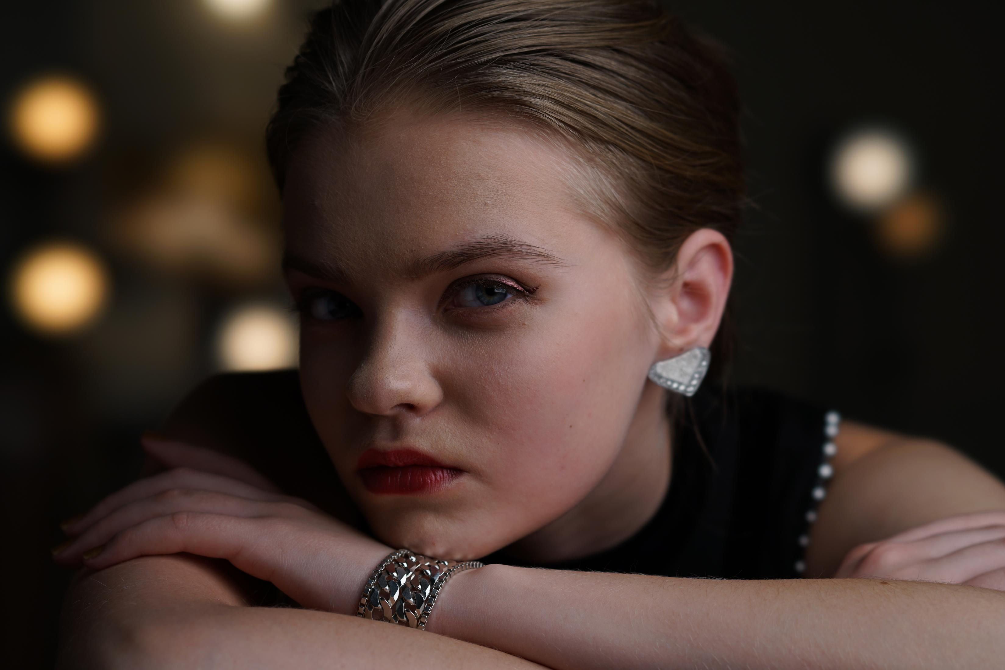 Une femme avec du rouge à lèvres rouge et un bracelet argenté, regardant la caméra.
