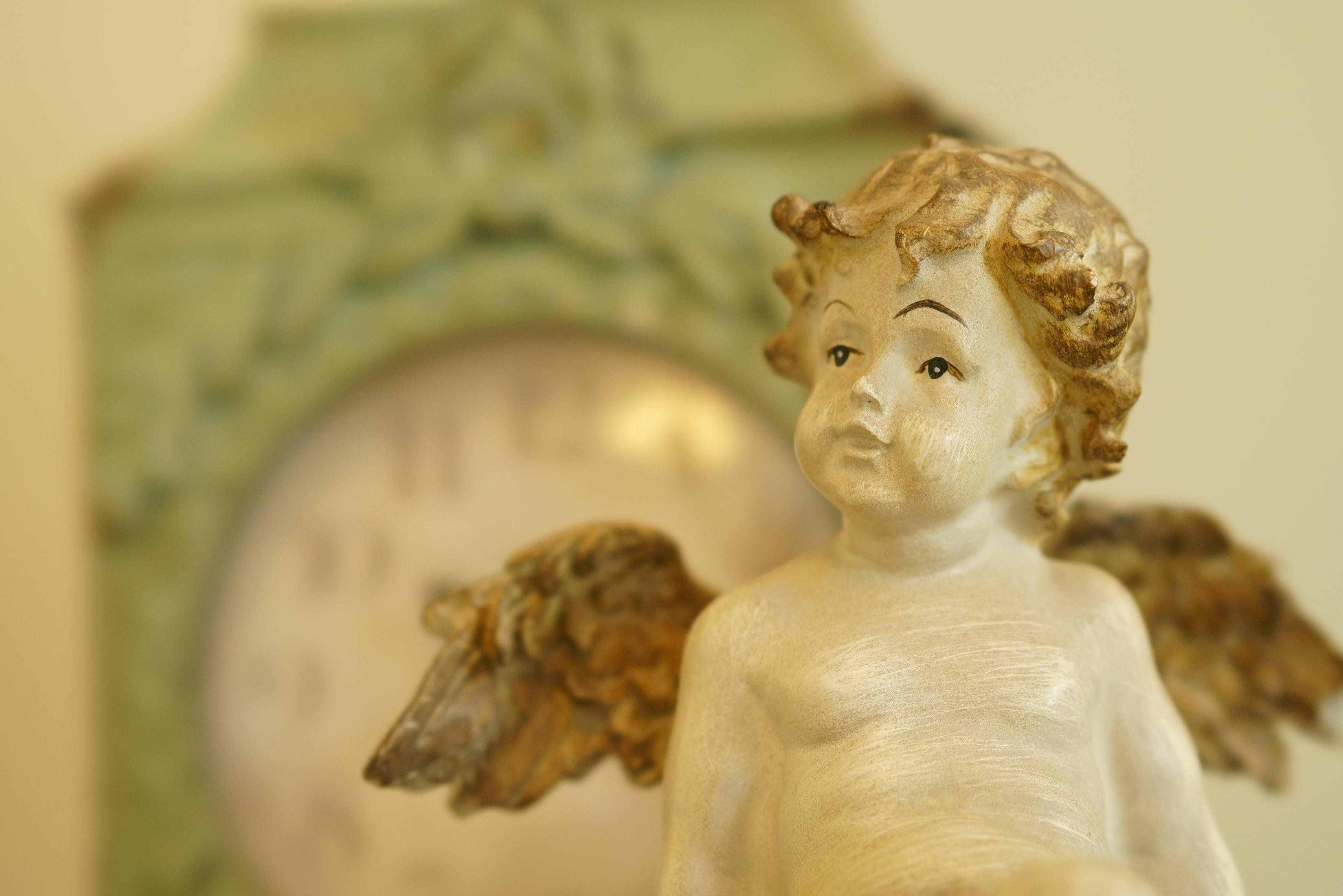 Une petite statue de chérubin avec des ailes devant une horloge antique floue.