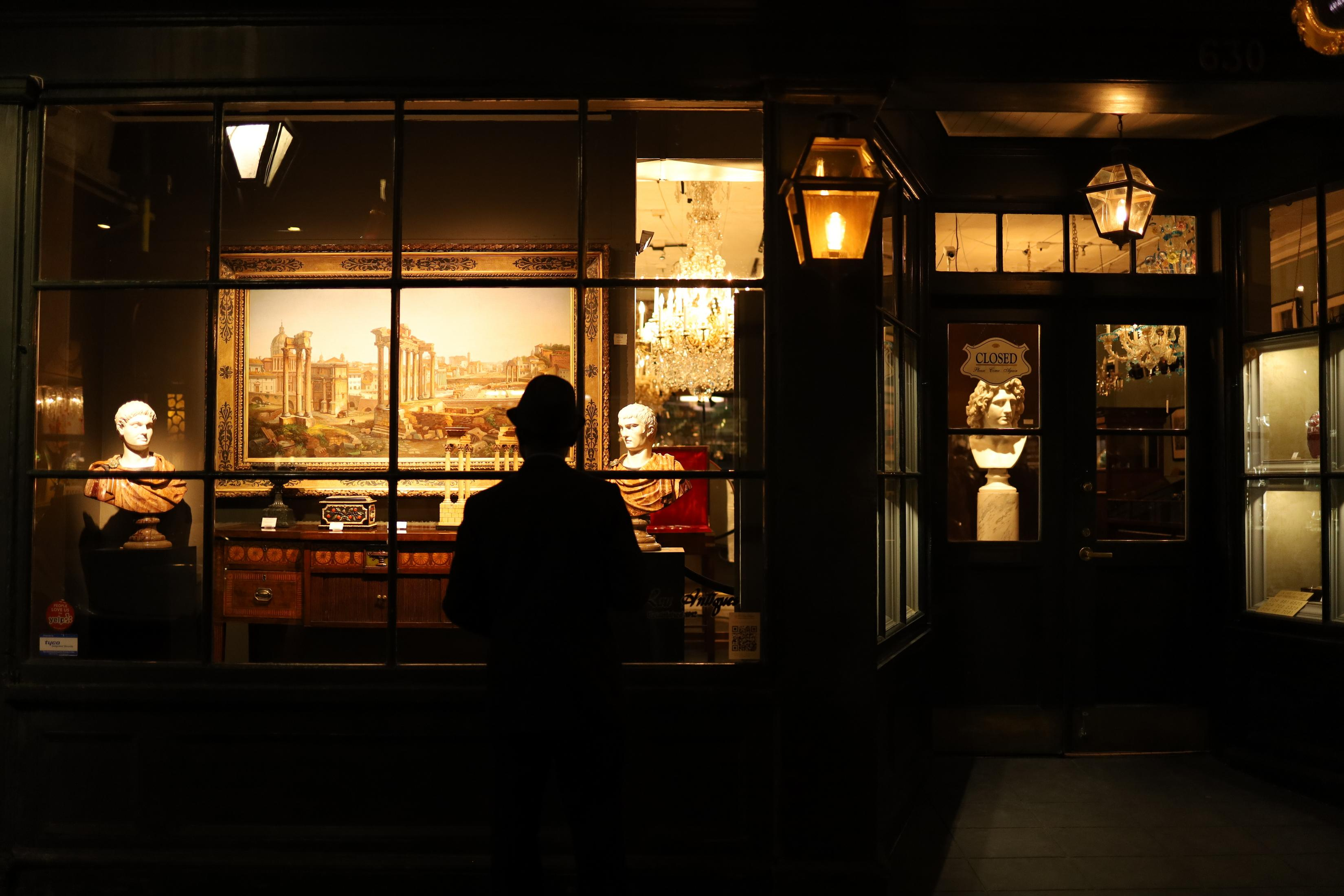 Personne dans une entrée de magasin regardant une vitrine. Statues et peinture à l'intérieur.