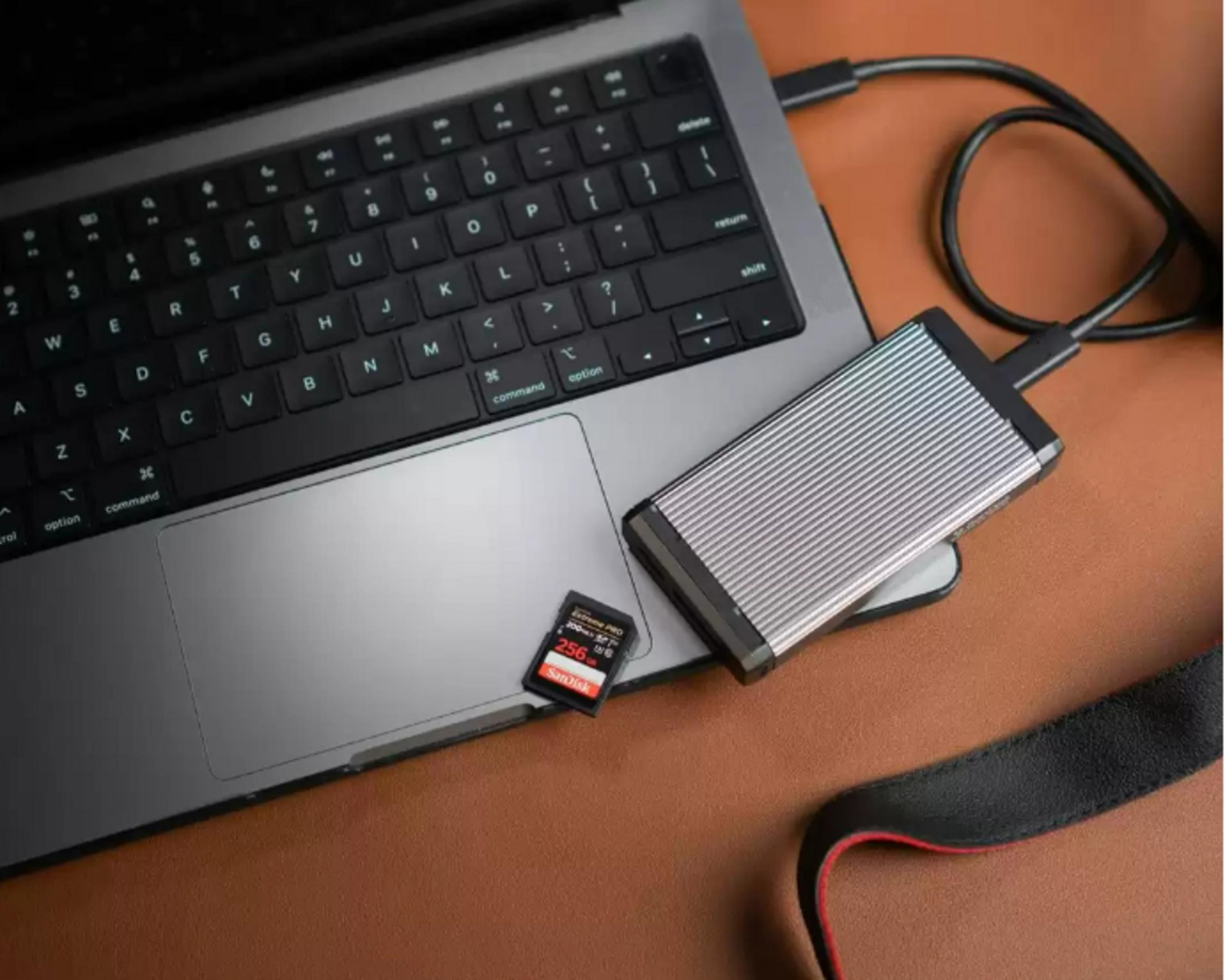 Laptop z podłączonym dyskiem zewnętrznym. Karta SD na gładziku. Brązowa powierzchnia.